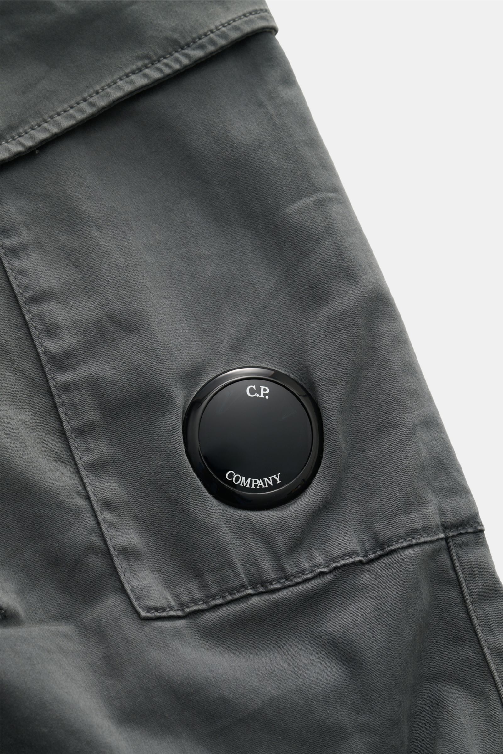 Close-up front view of the C.P. Company Cargohose dunkelgrau in dark gray gabardine cotton, showing the label-typical black lens detail on the cargo pocket. Urban Utility: Die Cargohose von C.P. COMPANY kombiniert funktionale Details mit entspanntem Fit u