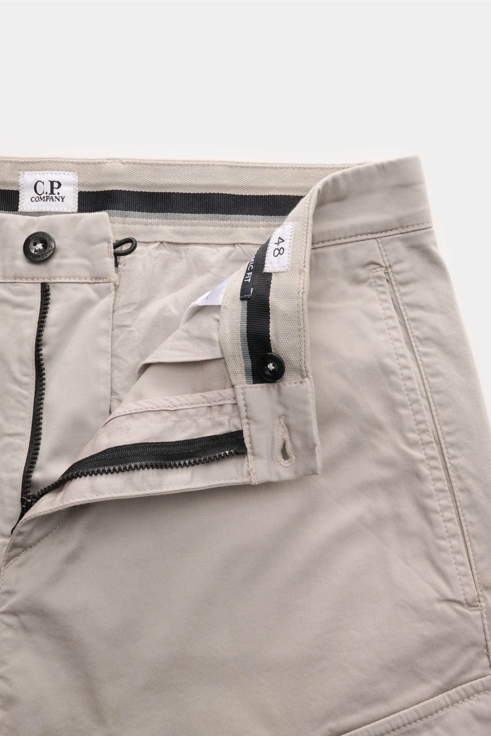 Close-up front view of C.P. Company Cargohose hellgrau showing open zipper, button, and waistband details in light grey cotton gabardine. 

Urban Utility: Die Cargohose von C.P. COMPANY kombiniert funktionale Details mit entspanntem Fit und hohem Komfo