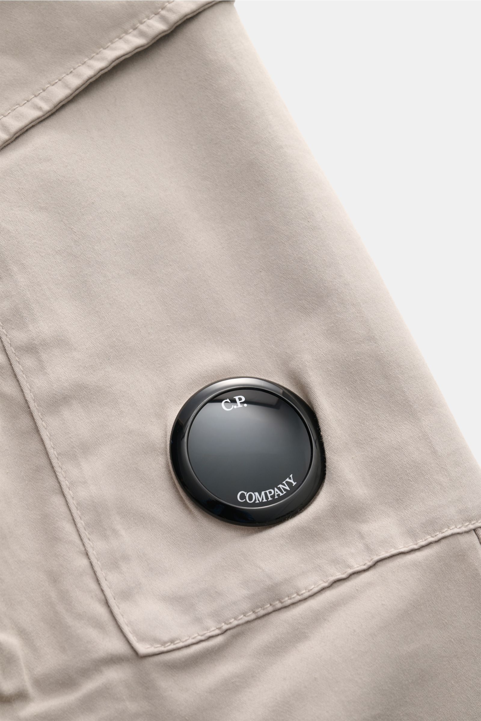 Close-up side view of C.P. Company Cargohose hellgrau fabric and black lens detail on the cargo pocket. Urban Utility: Die Cargohose von C.P. COMPANY kombiniert funktionale Details mit entspanntem Fit und hohem Komfort. Gabardine aus Baumwolle, komfortabl