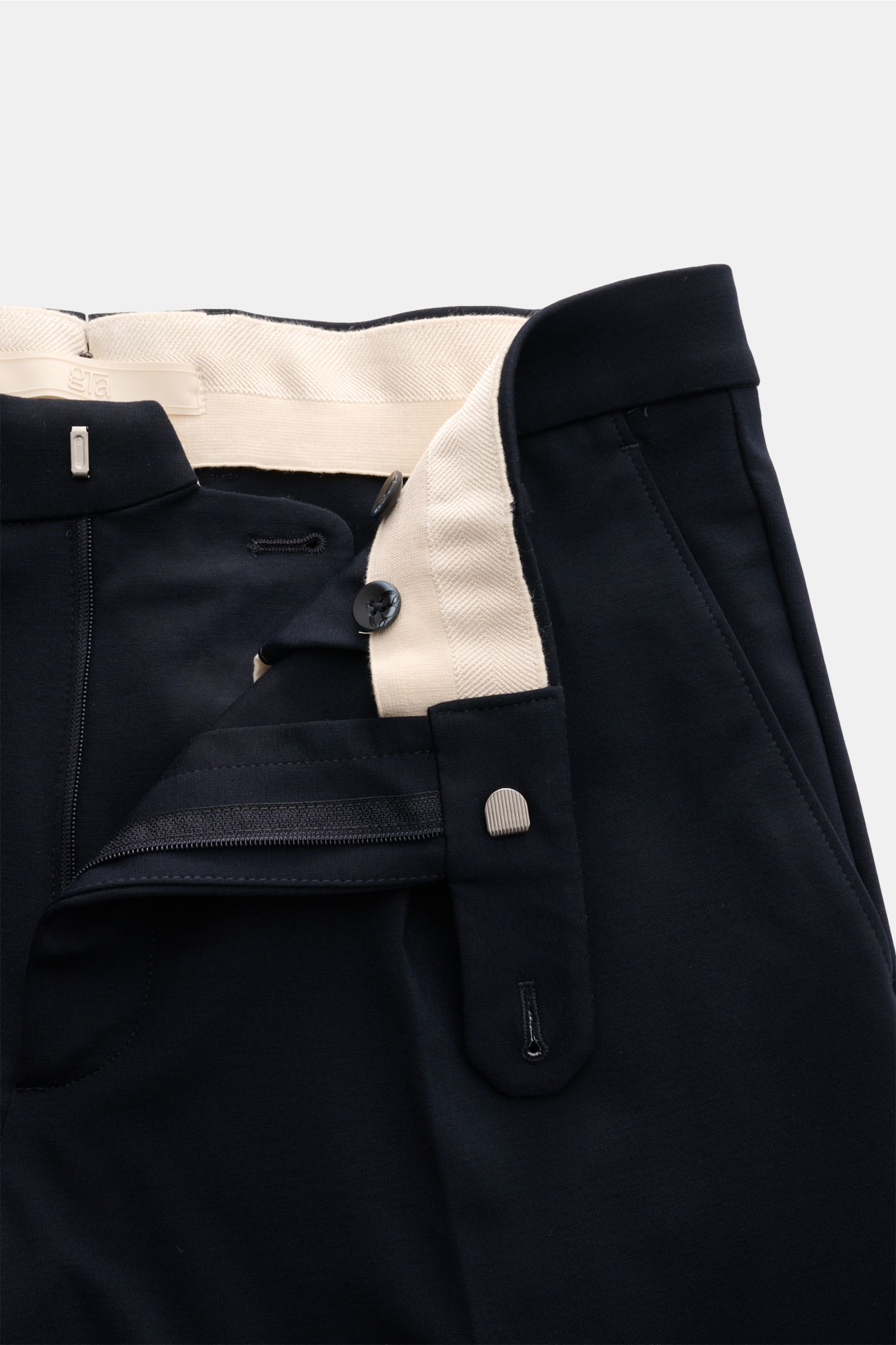 Close-up front view of navy GTA Jersey trousers 'Federico' showing open waistband with elastic insert, zip, button, single pleat, French pockets, and soft jersey fabric made of viscose and microfiber, designed for casual office looks with a slightly taper