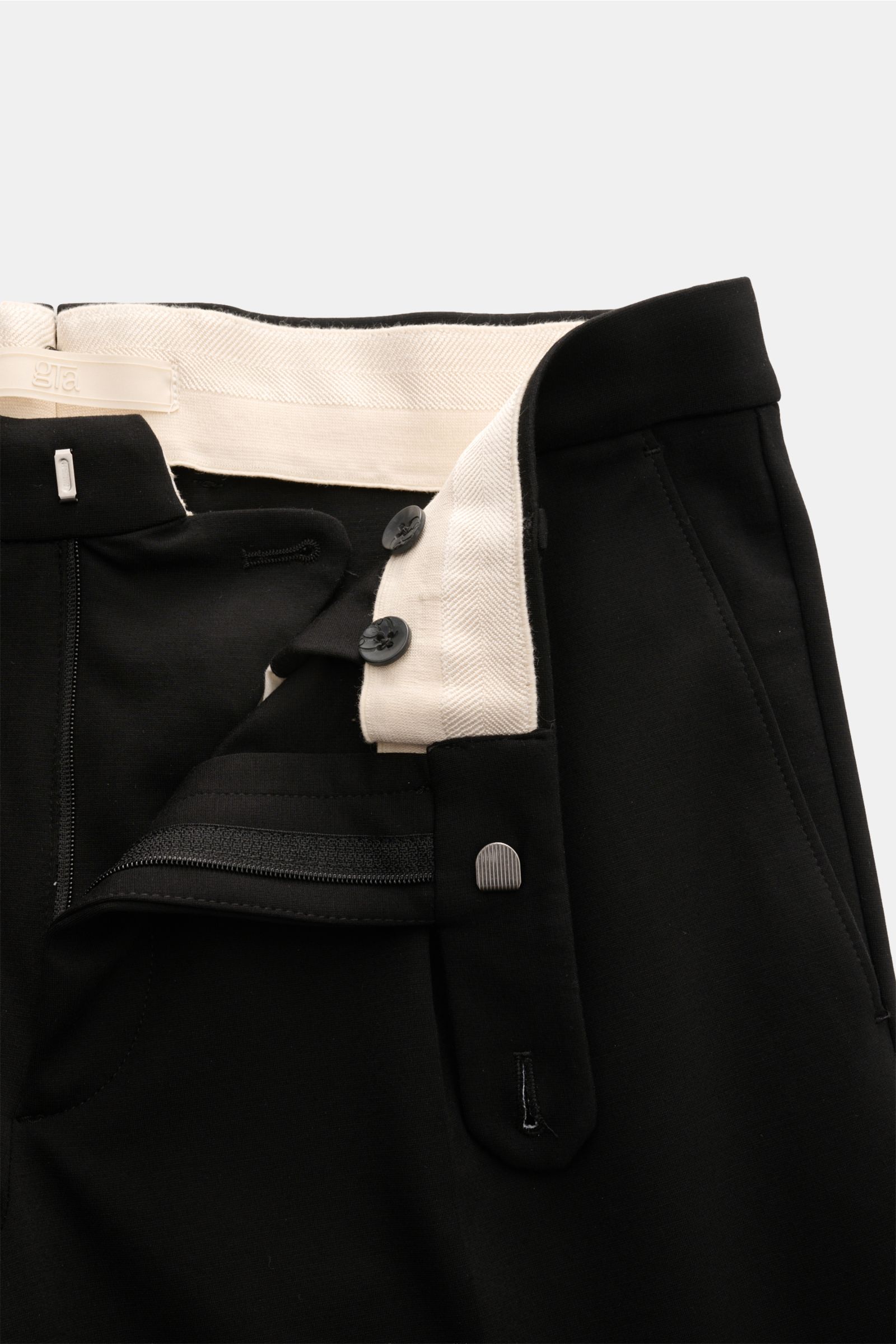 Close-up top-front view of GTA Jersey trousers 'Federico' black, showing elastic waistband, zip, buttons, single pleat, French pockets, and soft jersey fabric. For casual office looks: The jersey trousers 'Federico' by GTA combine maximum comfort with tim