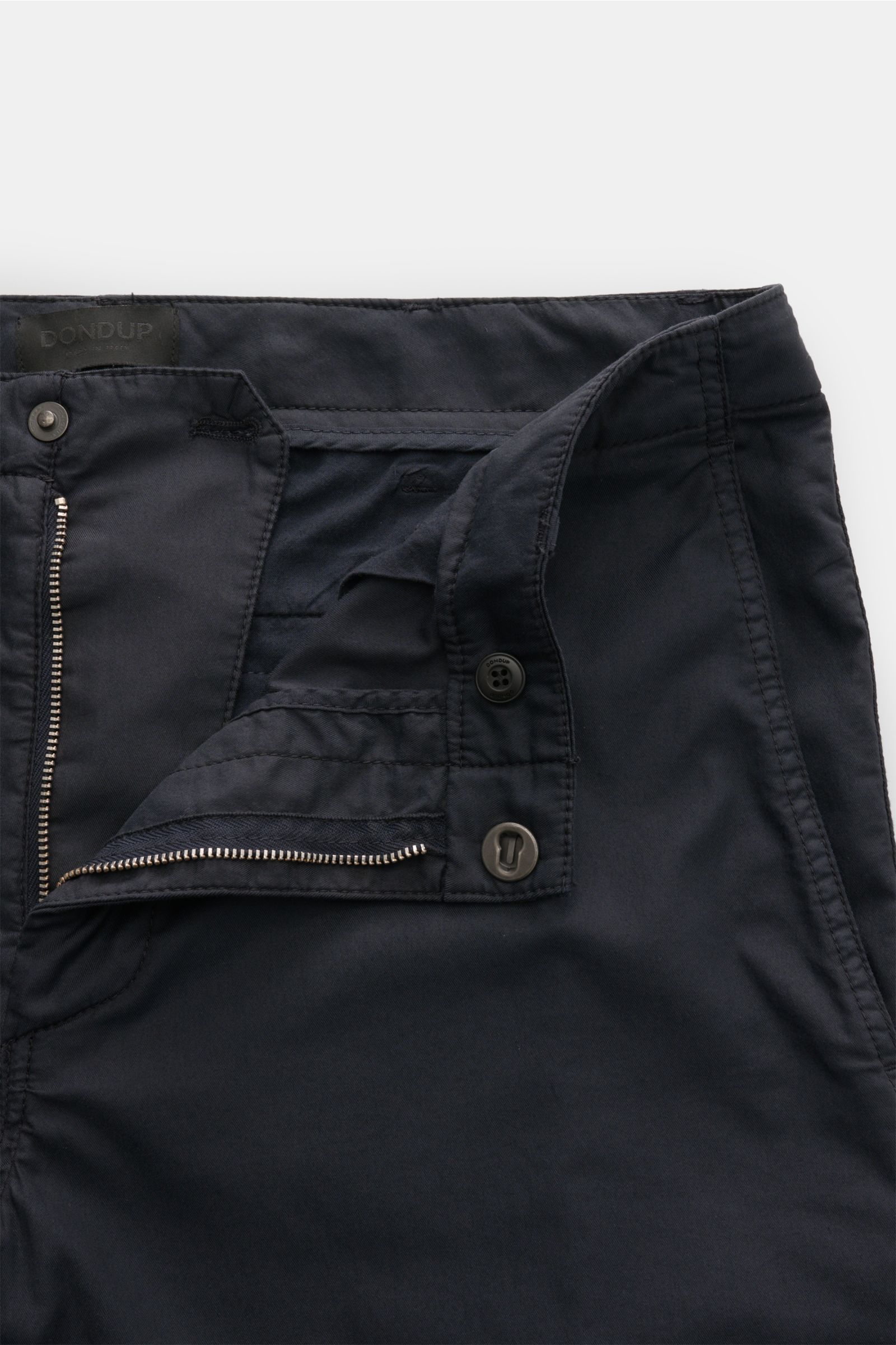 Close-up front view of Dondup Chino 'Zyan' dark navy with zipper, button closure, and clean stitching showing slim fit cotton-microfiber mix.

Description: Smart Casual mit Komfort: Die Hose 'Zyan' von DONDUP kombiniert klare Schnittführung mit elastis