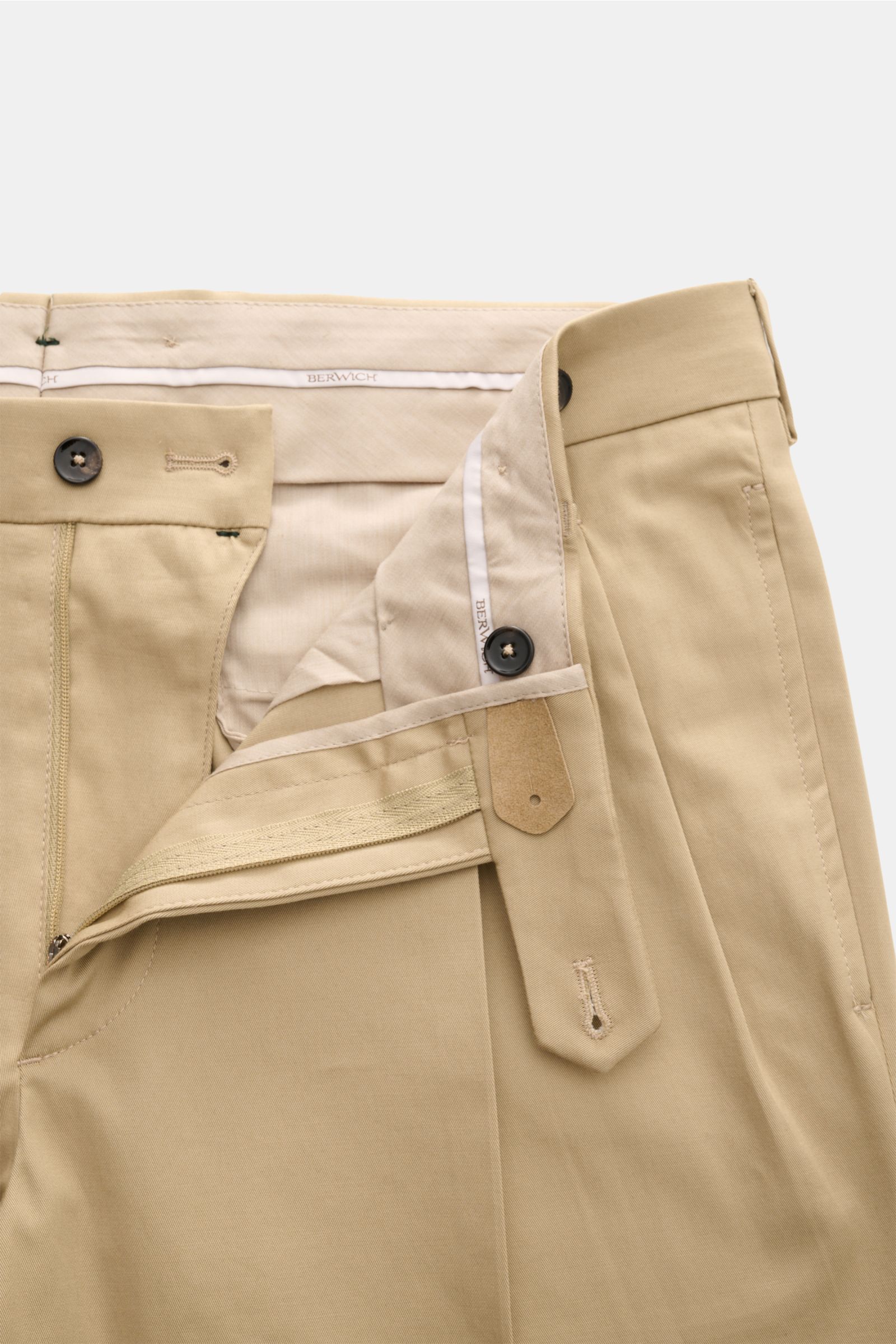 Close-up front view of Berwich Chino 'Barber' beige pants made from cotton twill with stretch, featuring double pleats, buttons for suspenders, zip fly, side and back pockets, fixed cuff, and extended button tab.

Description: Die Chino 'Barber' von BE