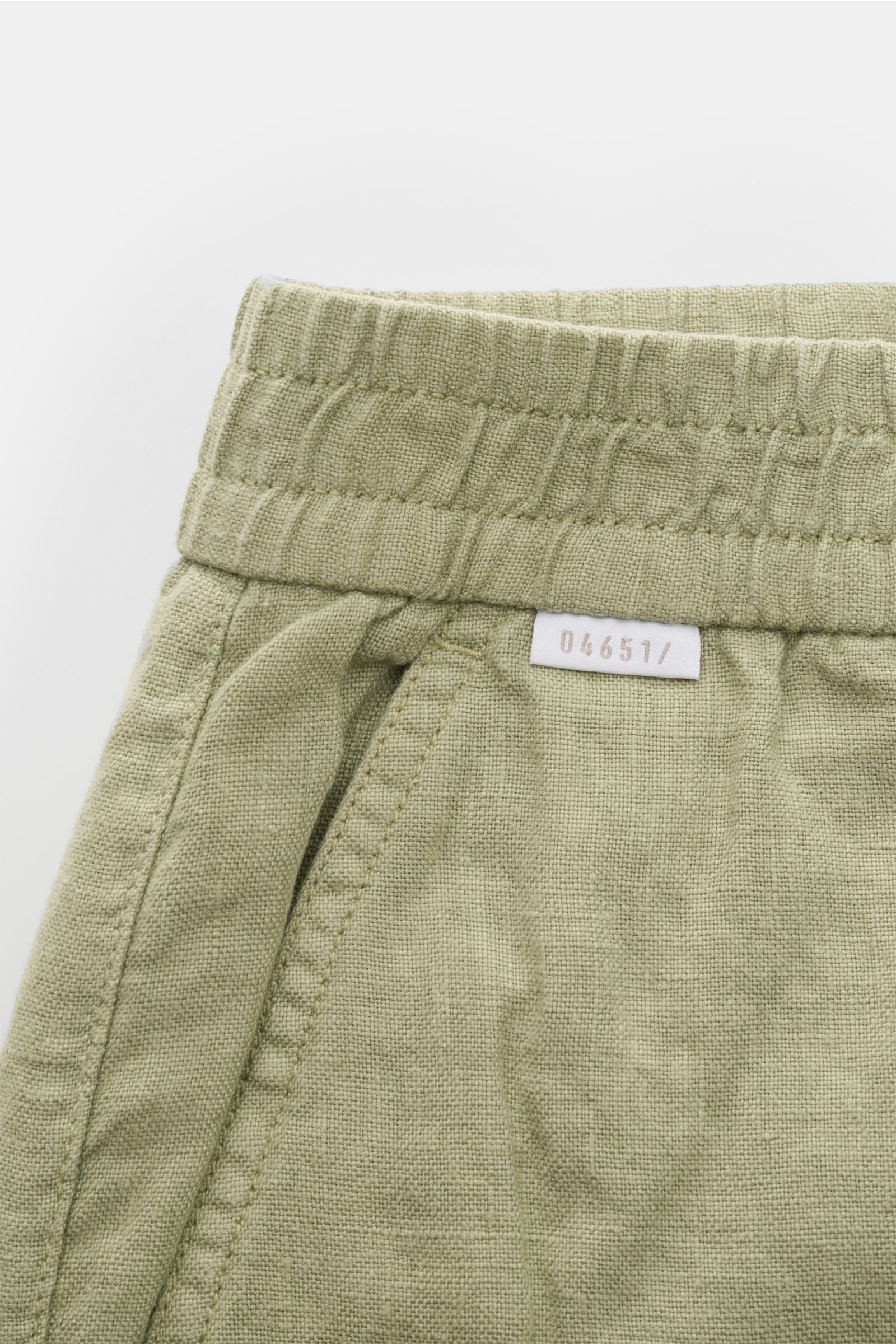 Nahaufnahme der salbeigrünen 04651/ A trip in a bag Leinen-Jogpants 'Linen Pants' mit elastischem Bund, französischer Tasche und Weblabel, typische Leinenstruktur sichtbar.