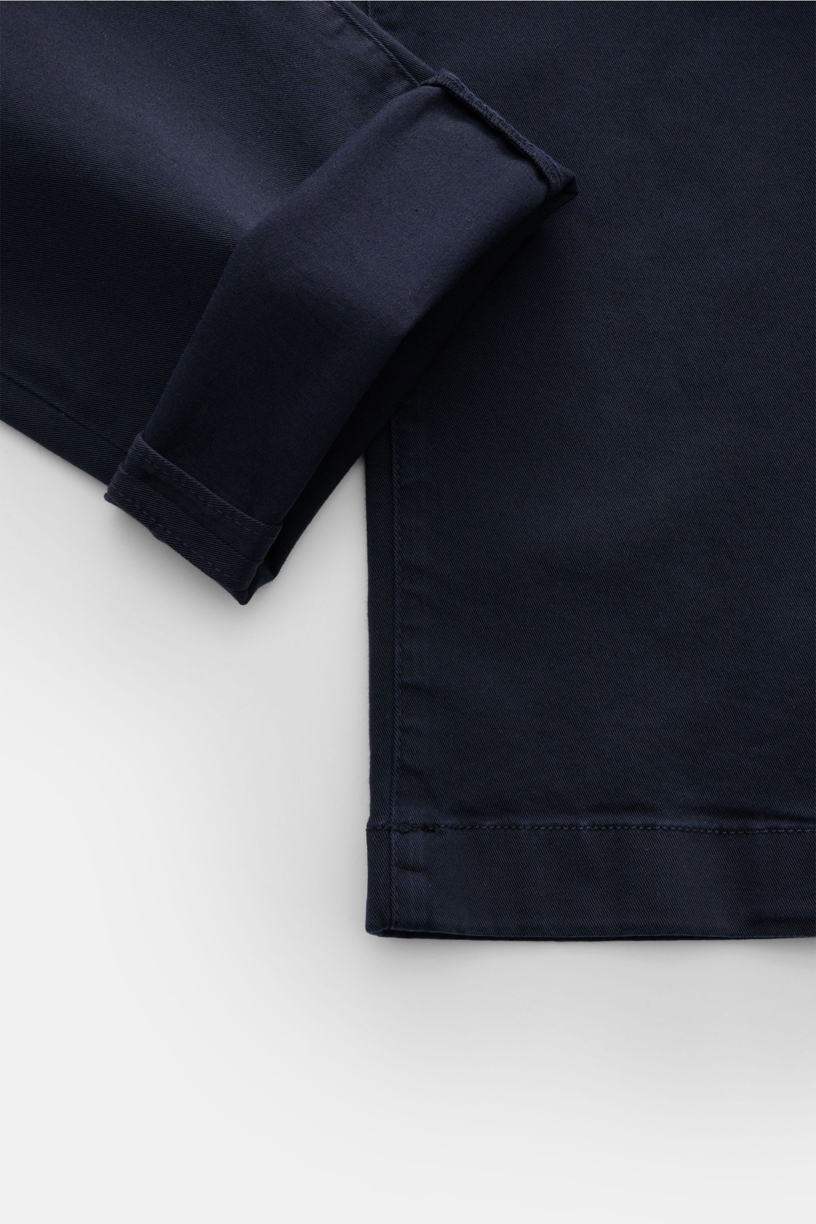 Close-up top-down view of the hem and cuff of the Jacob Cohen Chino 'Bobby' navy, showcasing slim fit, elastic pure cotton fabric, and tonal velour leather patch. Setzen Sie auf modernen Luxus im Alltag: Die schmal geschnittene Chino 'Bobby' von JACOB COH
