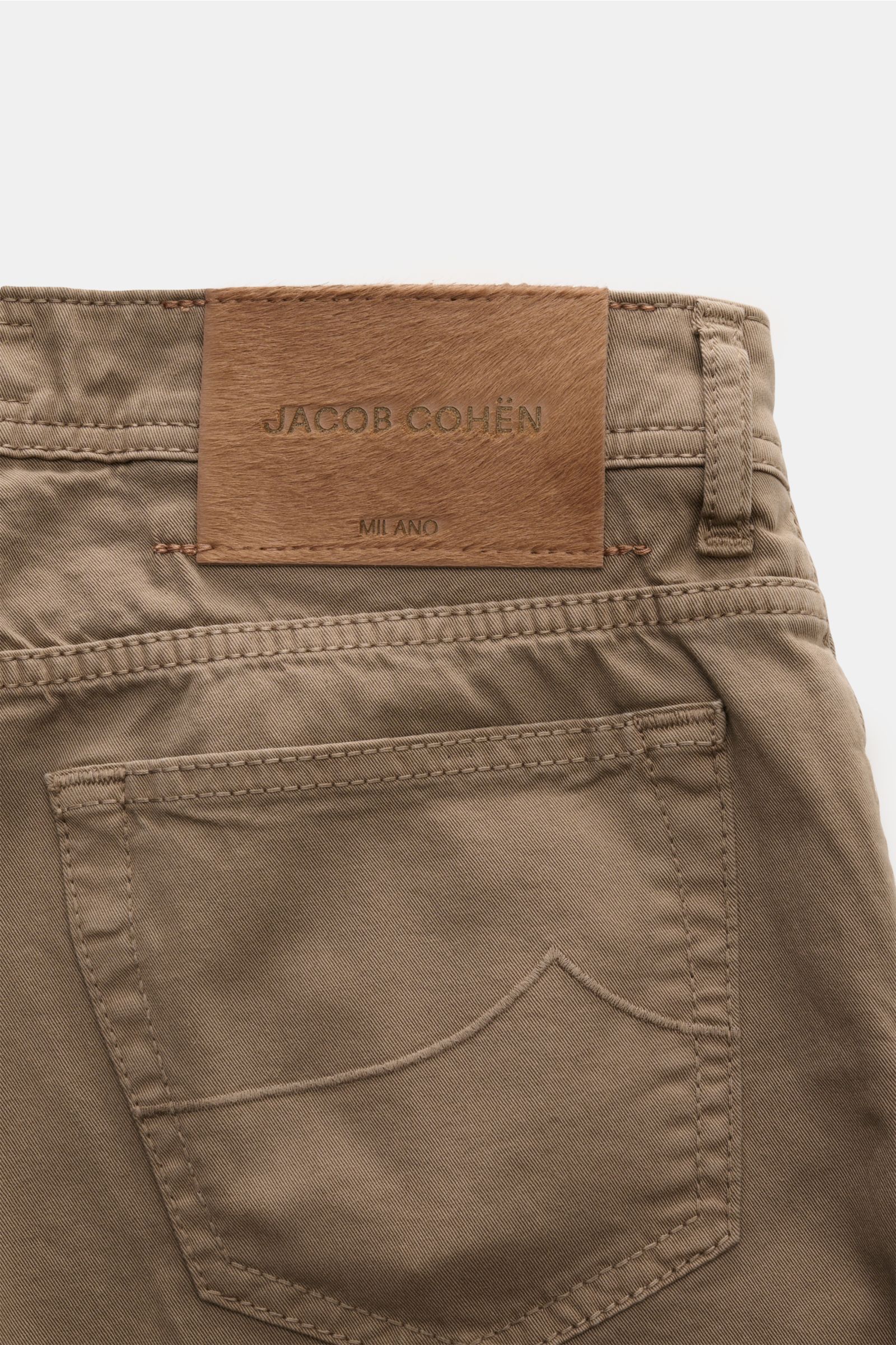 Close-up rear view of Jacob Cohen Baumwollhose 'Bard' graubraun showing high-quality elastic cotton fabric, slim fit, tonal stitching, five-pocket style, coin pocket with initial, button fly, and distinctive pony-fur leather patch. 

Description: Setze