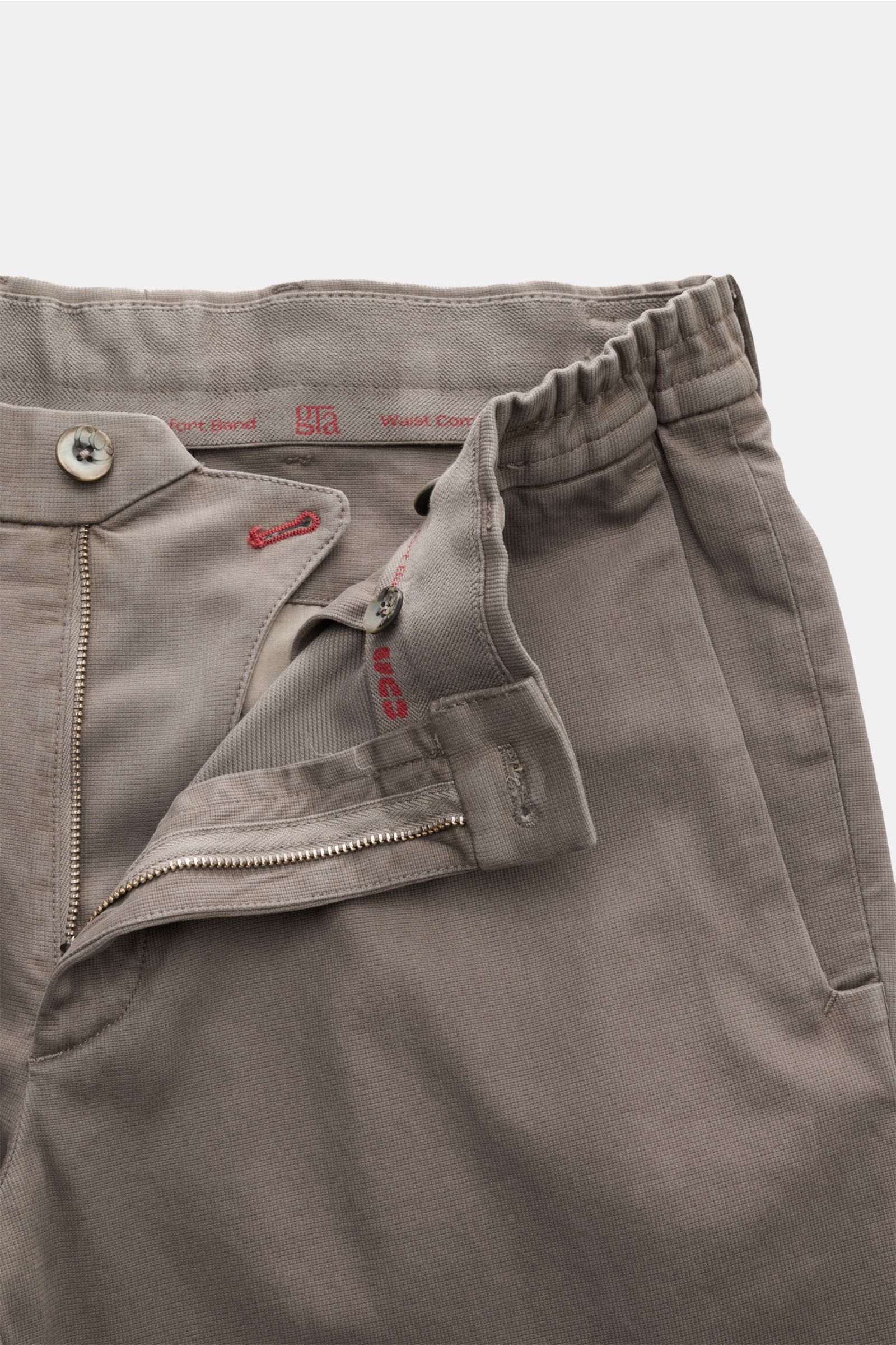 Close-up front view of GTA Trousers 'Dennis' grey-brown showing zip, button, elasticated waistband, and fabric texture.

Description: With the cropped, tapered trousers 'Dennis', GTA presents an essential that combines the relaxed feel of the internal Wai