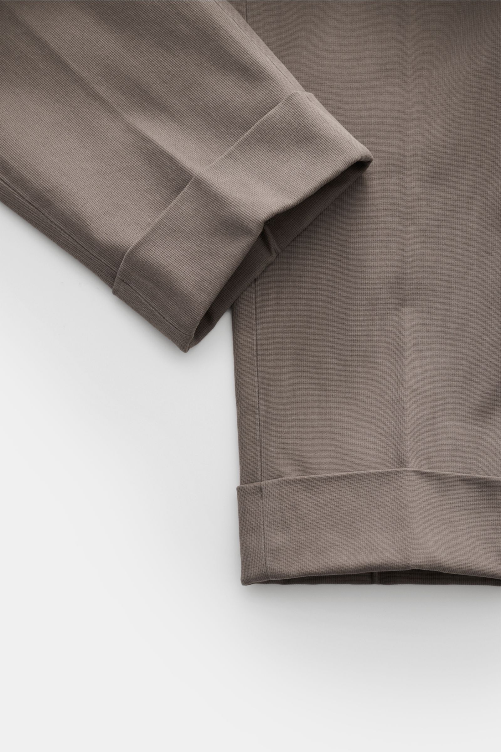 Close-up top view of folded GTA Trousers 'Dennis' grey-brown cropped tapered legs with fixed hem turn-up, showing fabric texture and seams. 

With the cropped, tapered trousers 'Dennis', GTA presents an essential that combines the relaxed feel of the i