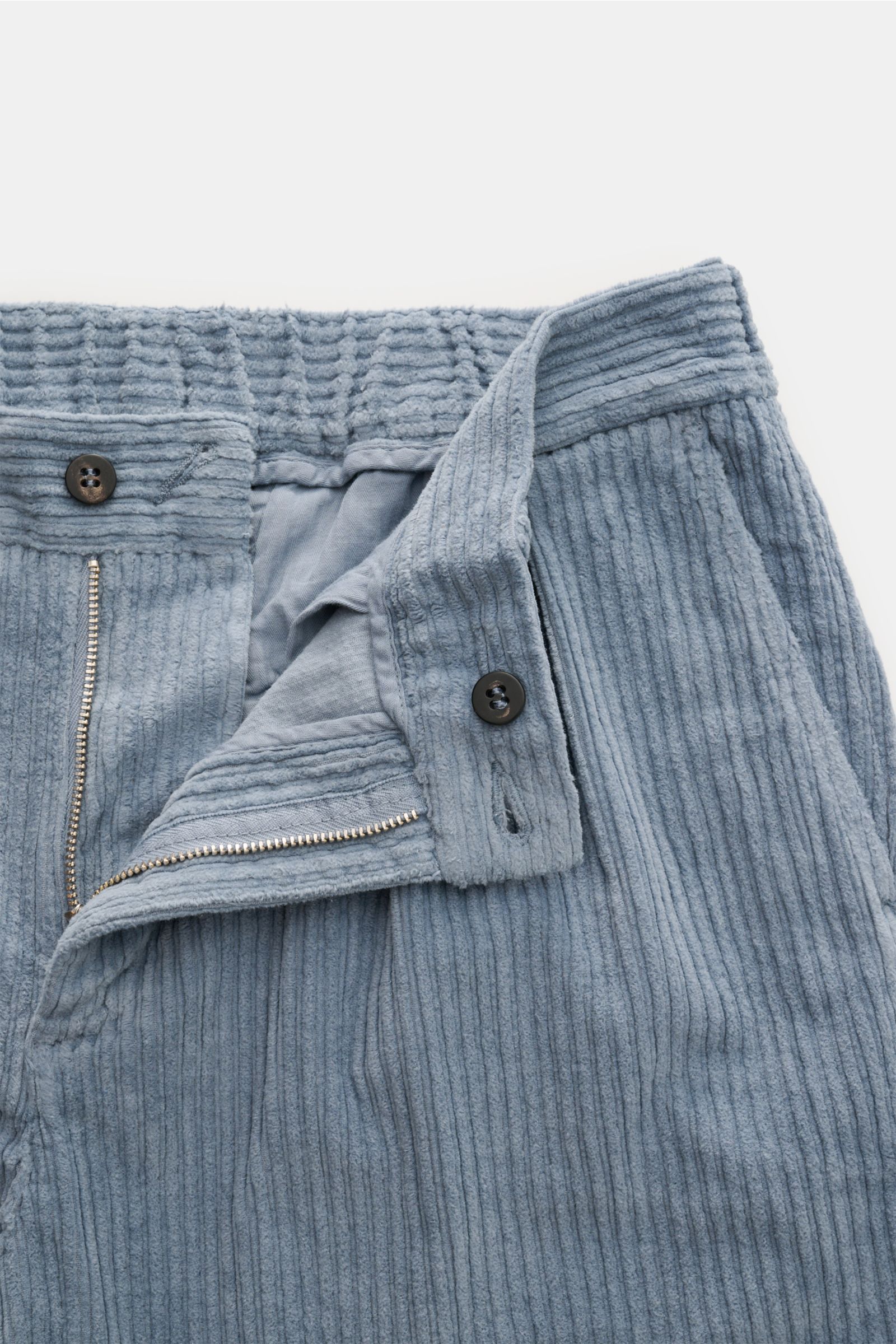 04651/ A trip in a bag Cordhose rauchblau, Detailaufnahme von Bund und Reißverschluss, elastische Baumwolle, weicher Griff, tapered Fit, knöchellang, schmal zulaufend.