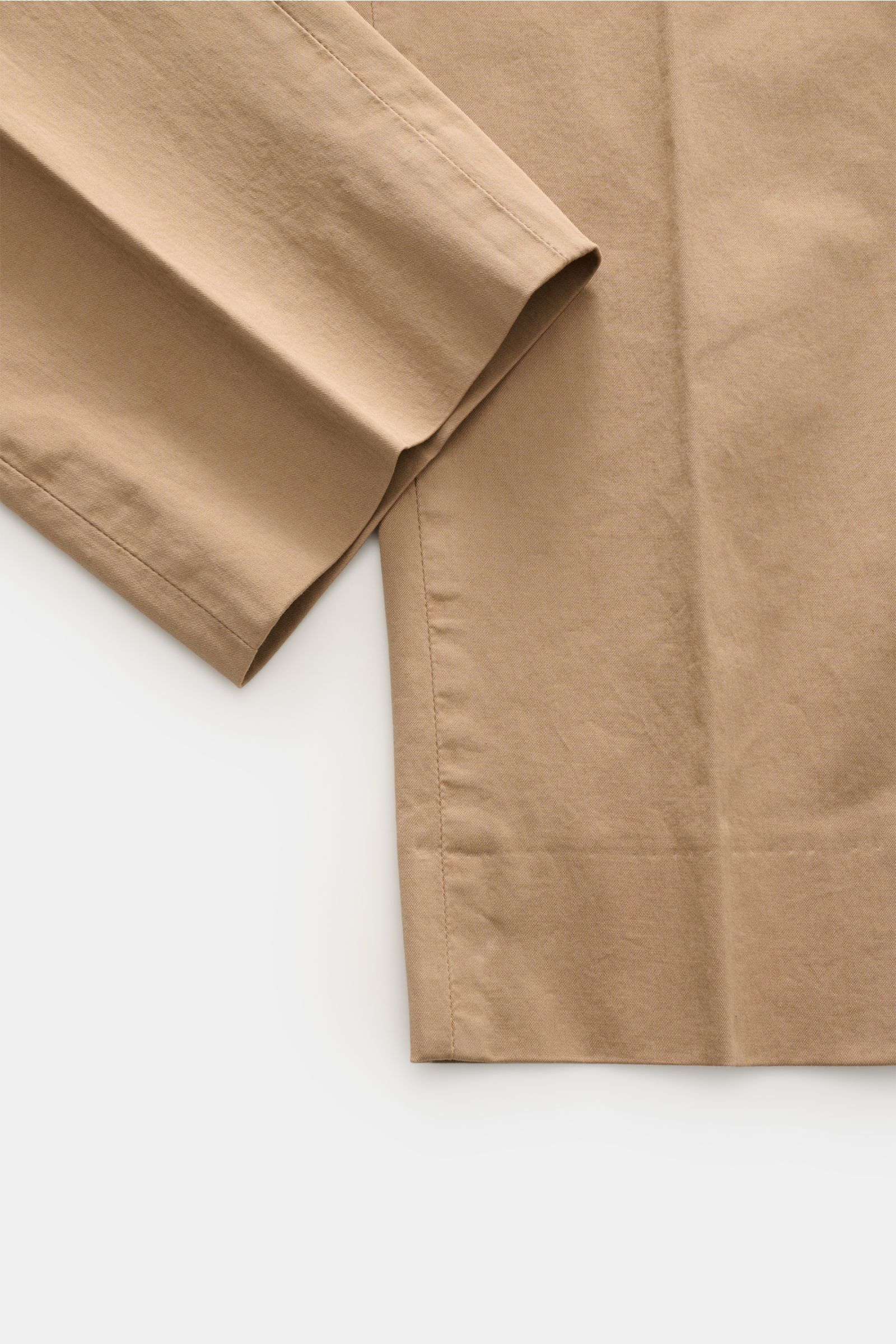 Close-up of the hem and lower leg of the GTA Chino 'Davide' hellbraun in light brown cotton twill, photographed from a top-down angle showing smooth fabric and fine stitching. 
