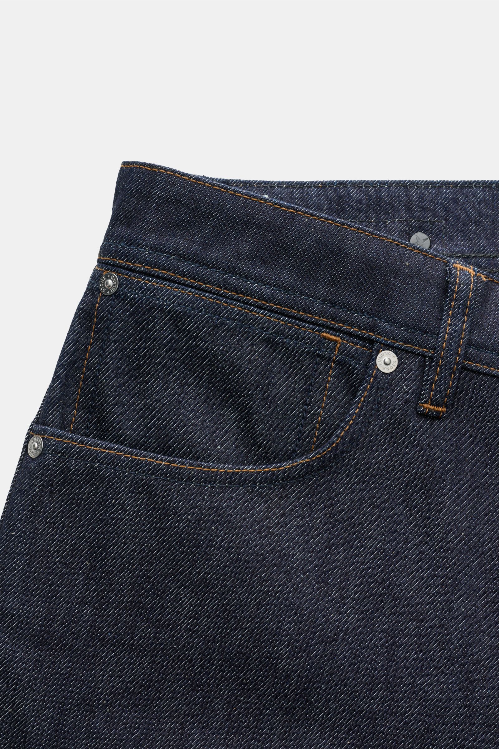 Nahaufnahme der Stone Island Jeans 'Indigo Denim - Raw' navy im Five-Pocket-Stil mit Loose Fit, Button Fly und Kompass-Badge am Bund, fotografiert von vorne schräg oben.