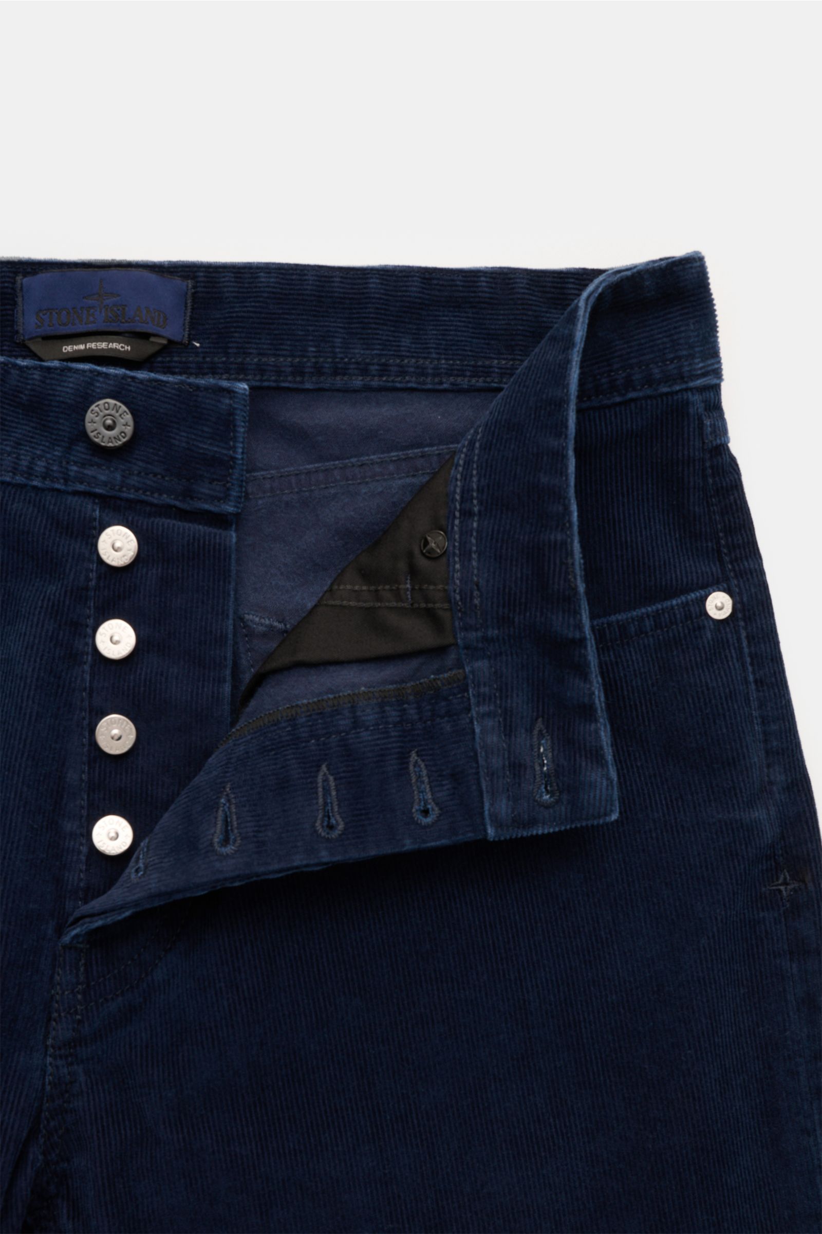 Front close-up of Stone Island Cordhose 'Micro Corduroy-Rinsed' navy showing button fly, buttonholes, and waistband with compass badge, made from cotton-microfiber blend corduroy.