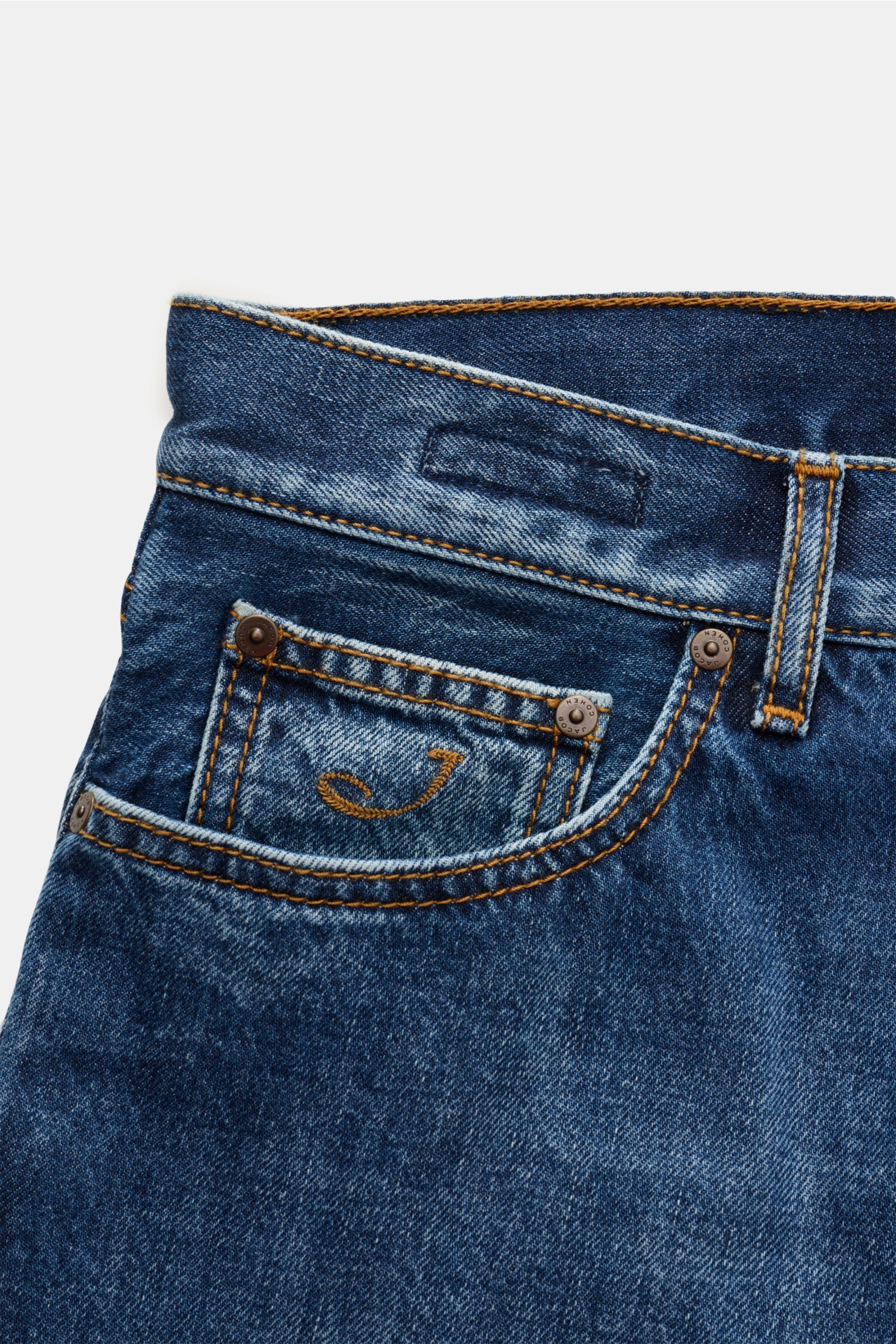 Close-up front view of Jacob Cohen Jeans 'Jude' blau in pure cotton denim with grippy texture, contrasting seams, button fly, five-pocket style, coin pocket with initial, back pockets with stitching, and vintage-look leather patch. Tapered fit, regular th