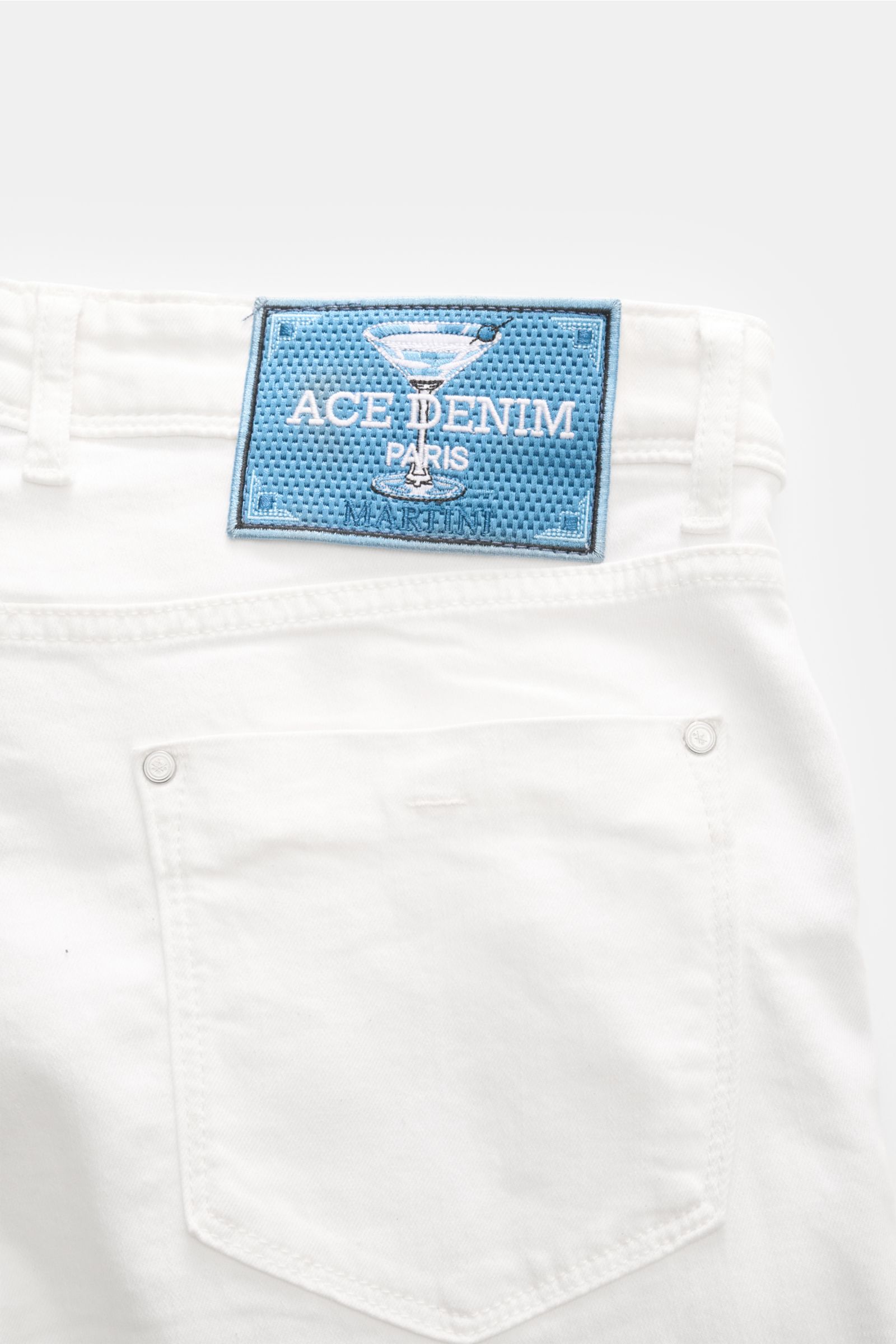 Close-up rear view of Ace Denim Jeans 'AD 15' off-white showing back pocket and blue woven patch with martini glass logo. ACE DENIM stands for hand-made jeans and sustainable production processes – the model 'AD 15' is made of a material blend with a slig