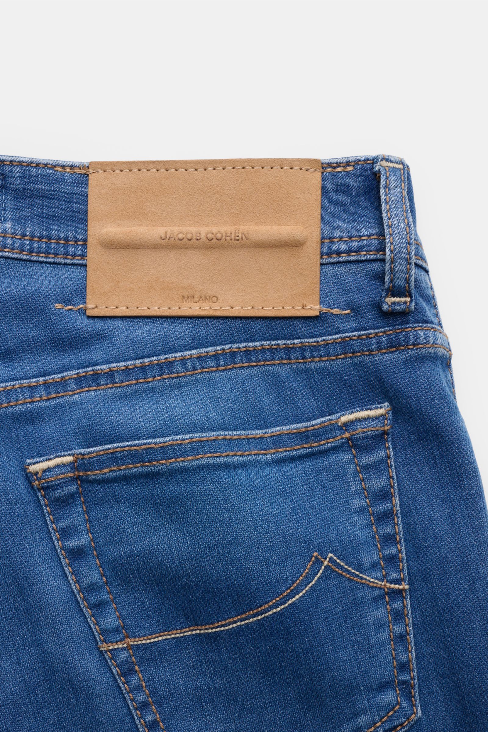 Close-up rear view of Jacob Cohen Jeans 'Bard' blau showing blue denim fabric, stitched back pocket, and tan leather patch with embossed logo. Modern luxury with a soft touch, slim fit, button fly, five-pocket style, coin pocket with initial, and detailed