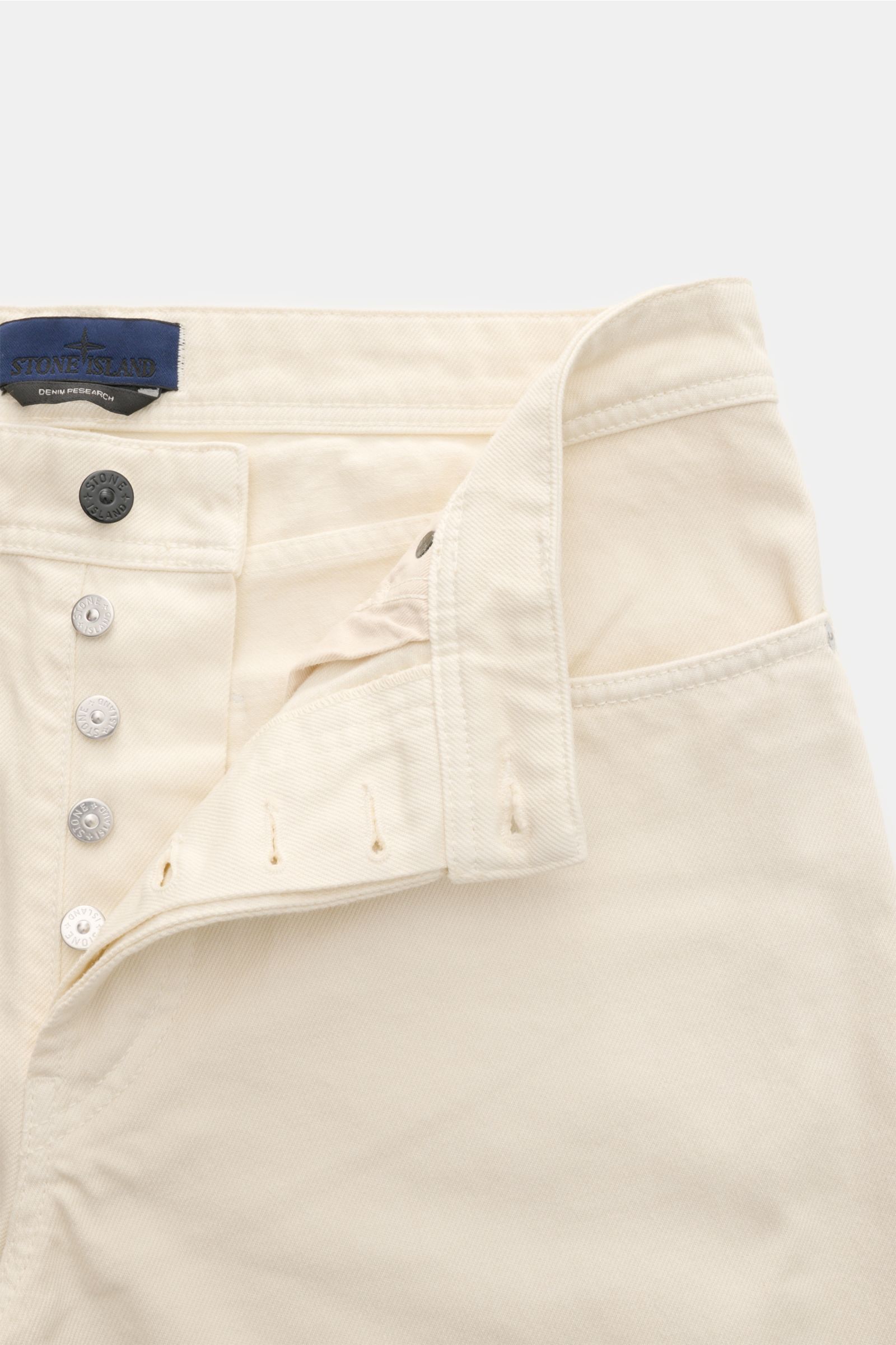 Stone Island Jeans 'Light Bull Denim' creme, Nahaufnahme vom Bund mit geöffneter Button Fly, Five-Pocket-Stil und Kompass-Badge.