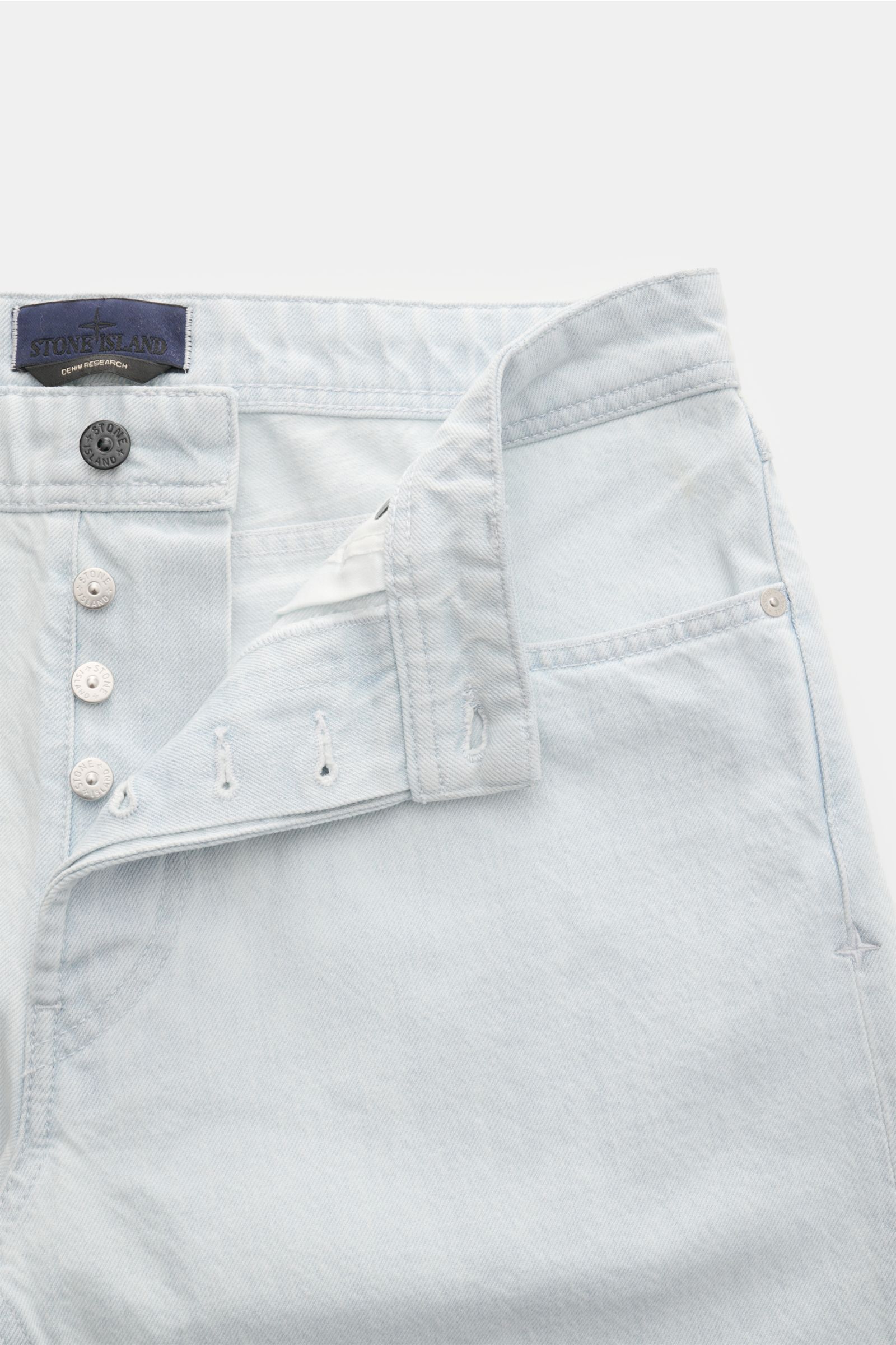 Stone Island Jeans 'Bleach' hellblau, frontale Nahaufnahme mit offenem Button Fly, geradem Schnitt, Five-Pocket-Stil, Kompass-Badge
