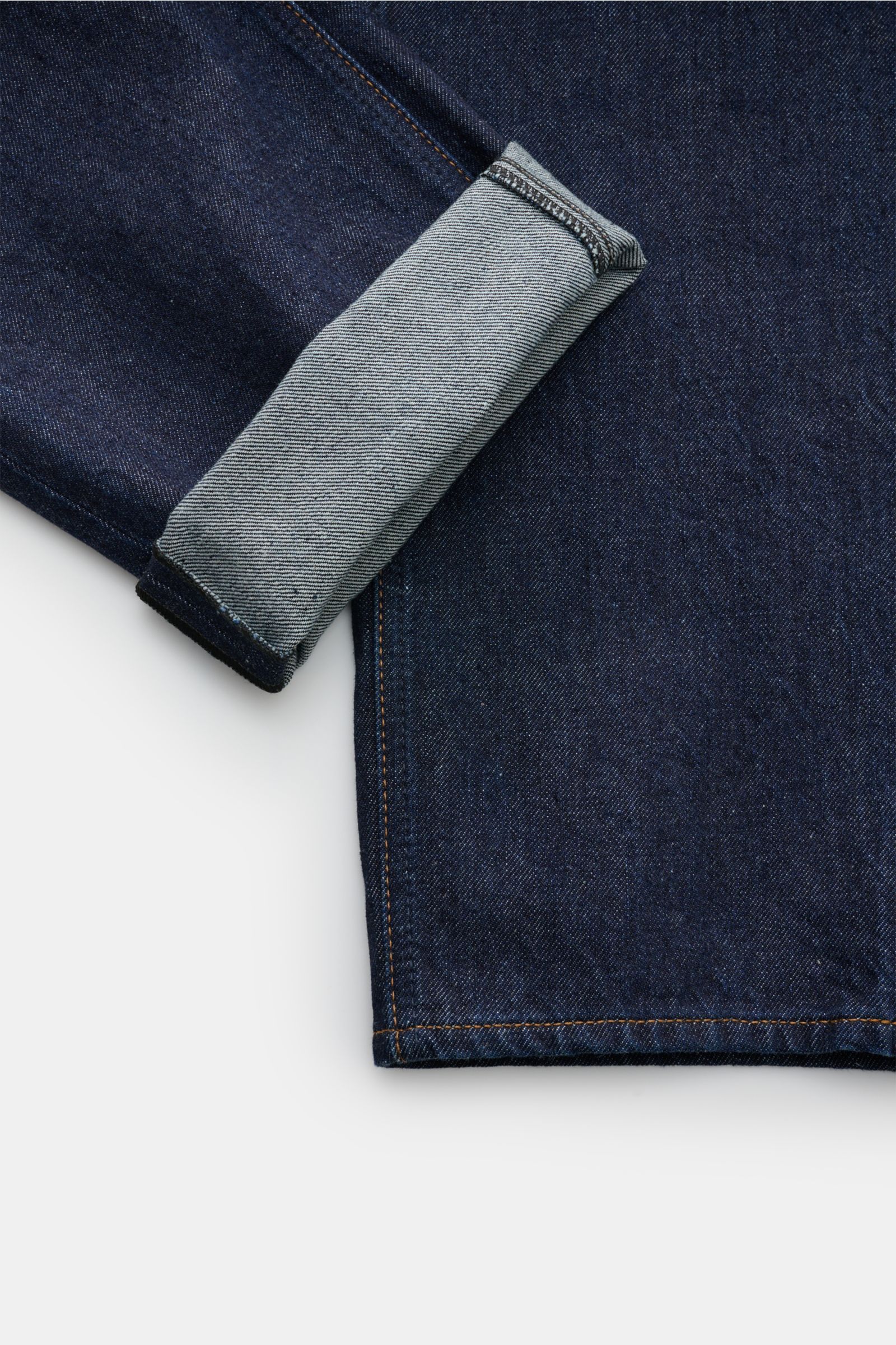 Close-up view of Stone Island Jeans 'Indigo Denim - Rinsed' dunkelblau showing dark blue denim fabric with folded cuff, straight fit, pure cotton, button fly, five-pocket style, and signature compass badge at the waistband. Urban classic in modern silhoue