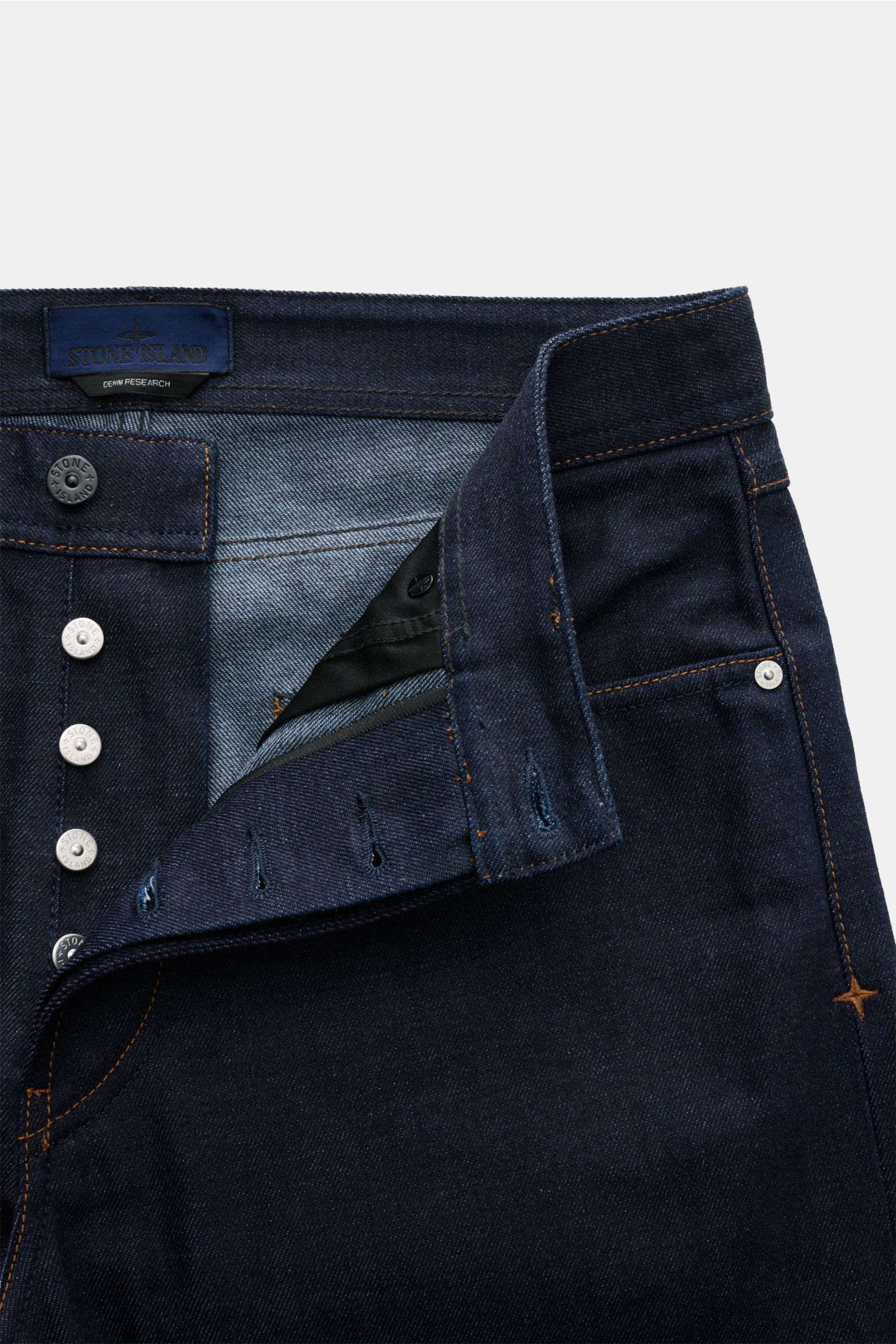 Stone Island Jeans 'Selvedge Indigo Denim - Raw' navy shown from a close-up top-front view with button fly, five-pocket style, and compass badge.