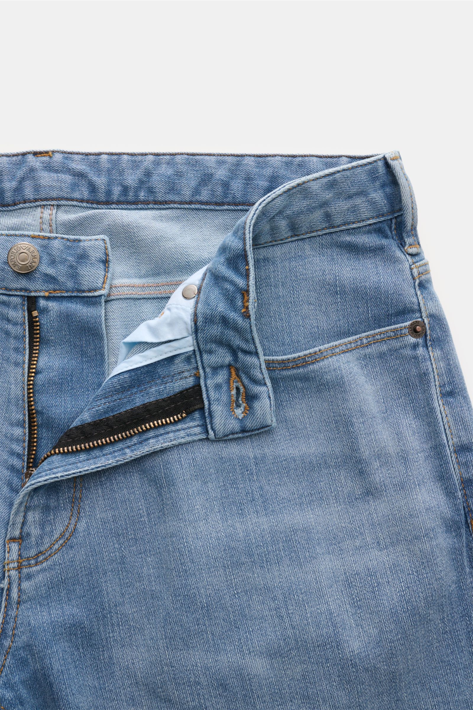 Close-up front view of Emporio Armani Jeans rauchblau with zip fly open, showing elastic cotton denim, slim fit, soft texture, five-pocket style, metal logos, and leather patch. Komfort trifft Stil: Die Jeans von EMPORIO ARMANI überzeugt durch angenehm