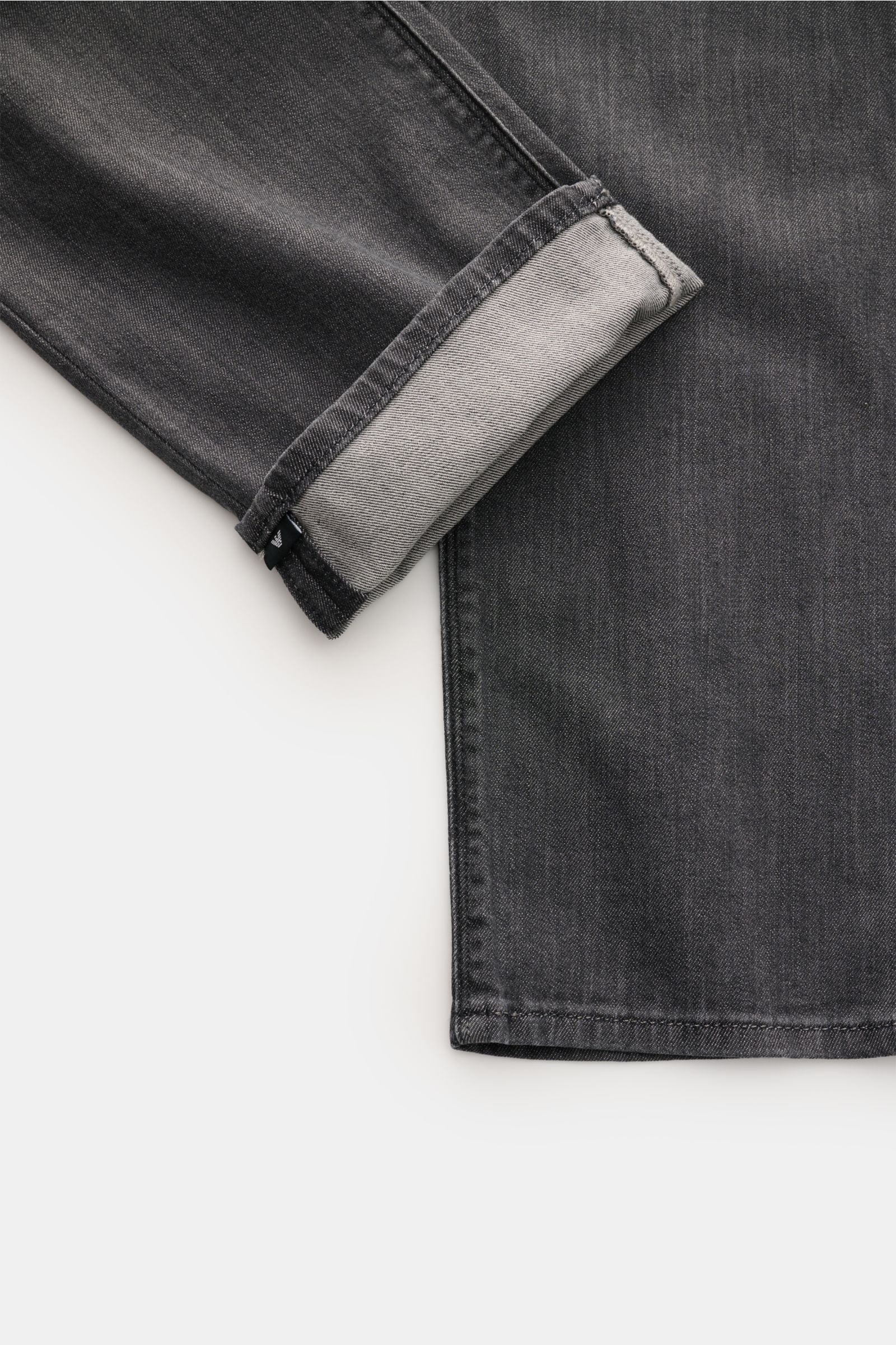 Emporio Armani Jeans dunkelgrau, Nahaufnahme vom Bein mit aufgekrempeltem Saum, Slim Fit, leichte Waschung, Metall-Logos, Lederpatch.