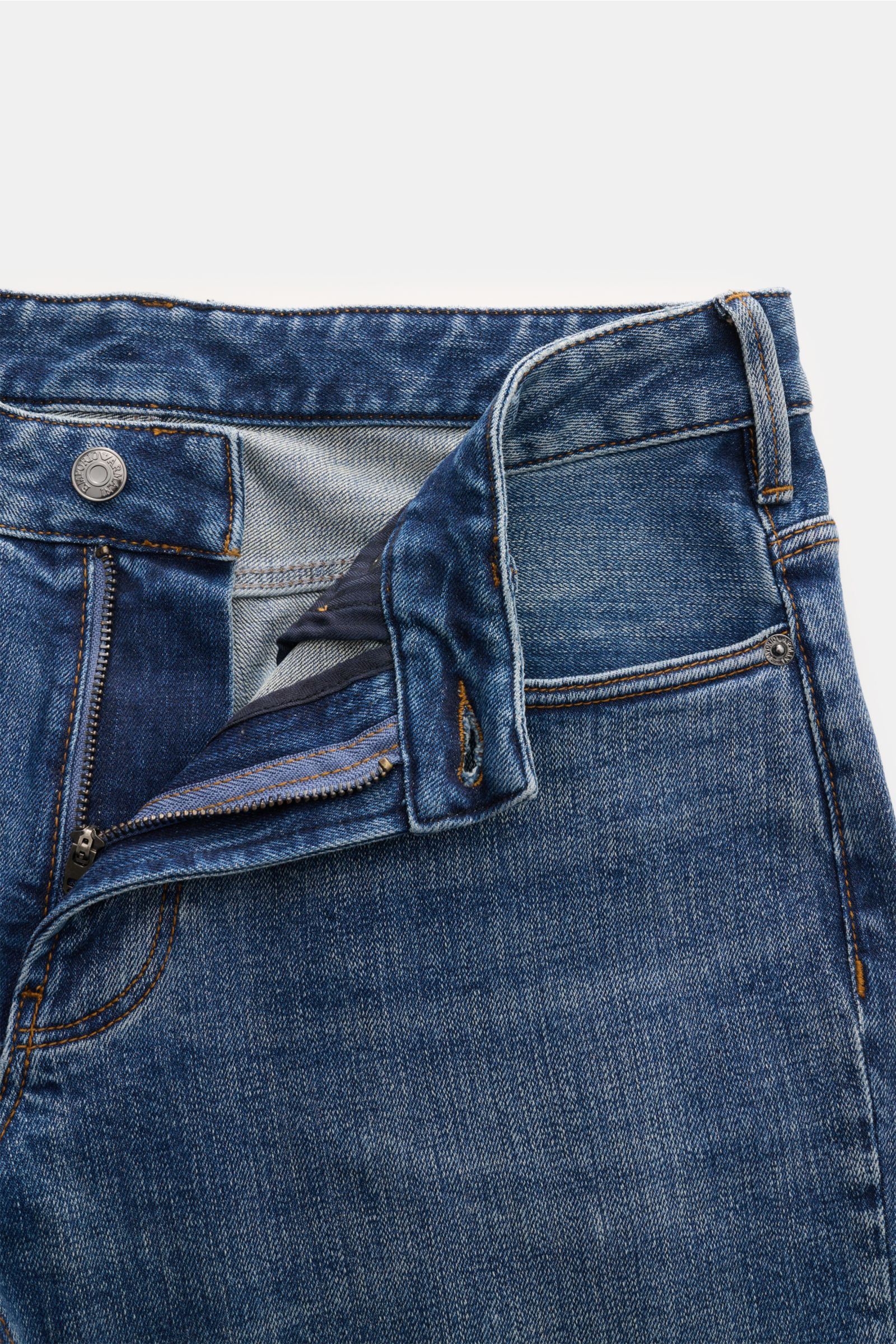 Emporio Armani Jeans blau, Slim Fit, Five-Pocket-Stil, kurzer Schnitt, Zip Fly, Metall-Logos, Leather Patch, Detailfoto von oben mit offenem Reißverschluss.