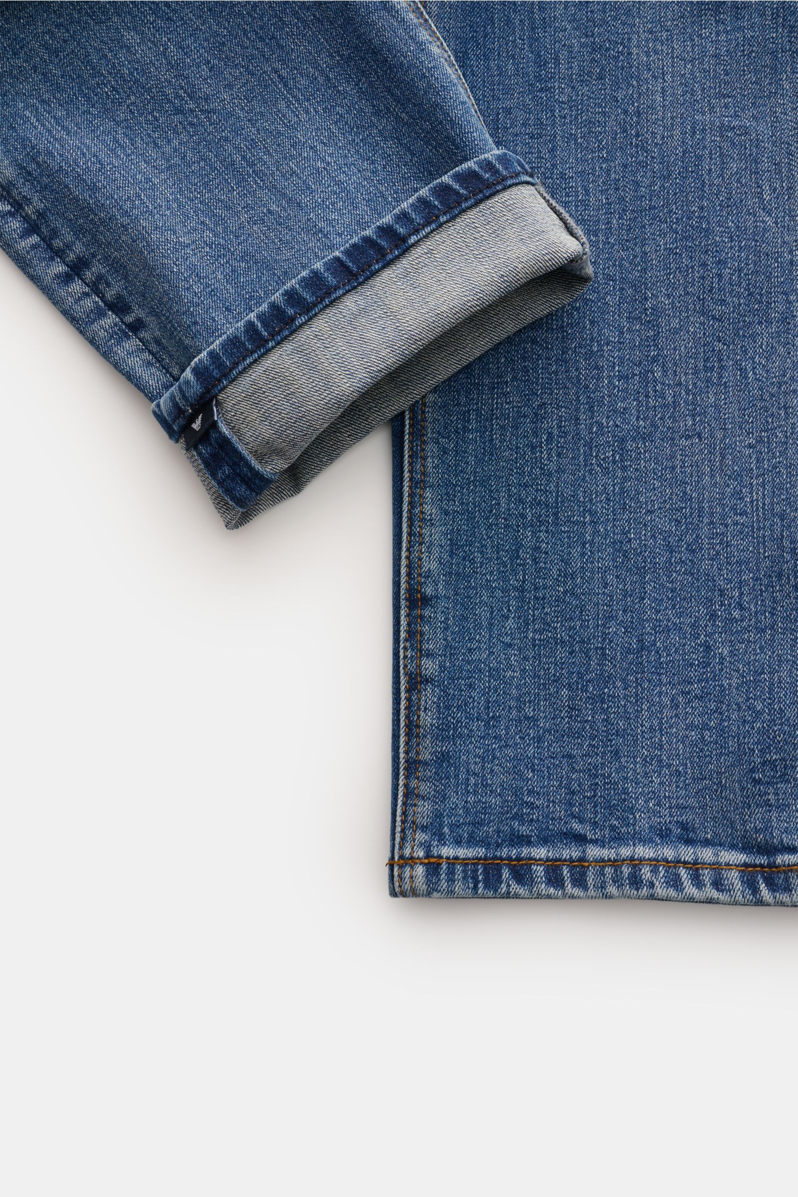 Nahaufnahme der Emporio Armani Jeans blau im Five-Pocket-Stil, Slim Fit mit kurzem Schnitt, authentischer Waschung und umgeschlagenem Saum, aus leicht elastischer Baumwolle für Komfort und Stil.