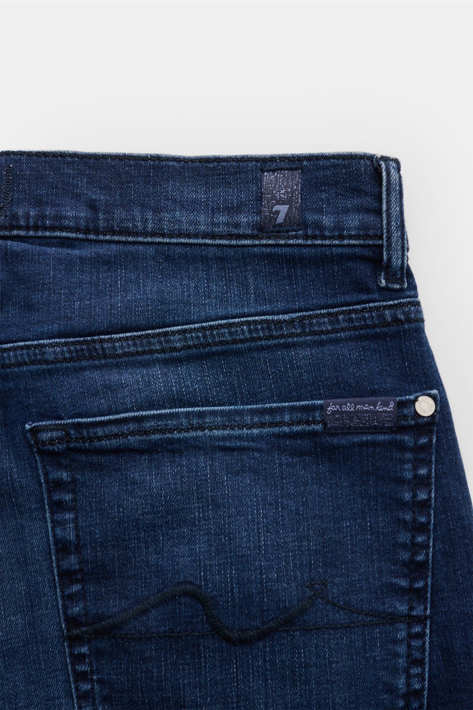 Close-up rear view of 7 for all mankind Jeans 'Slimmy' dark blue showing back pocket stitching, small woven label, and subtle used wash. Elasticated cotton, slim fit, slightly tapered cut, zip fly, five-pocket style. Seven pairs of jeans should be enough 