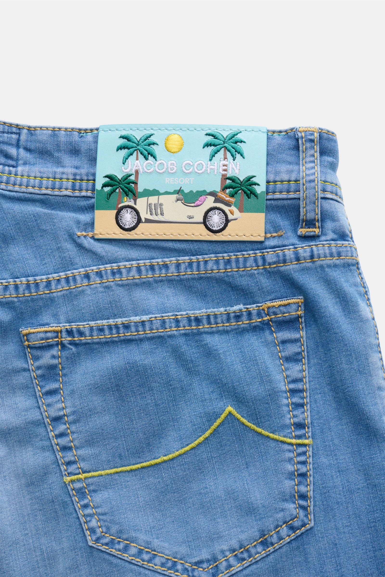 Jacob Cohen Jeans 'Bard' blau shown from the back, featuring a light blue leather patch with palm trees and a vintage car, soft denim with yellow stitching.