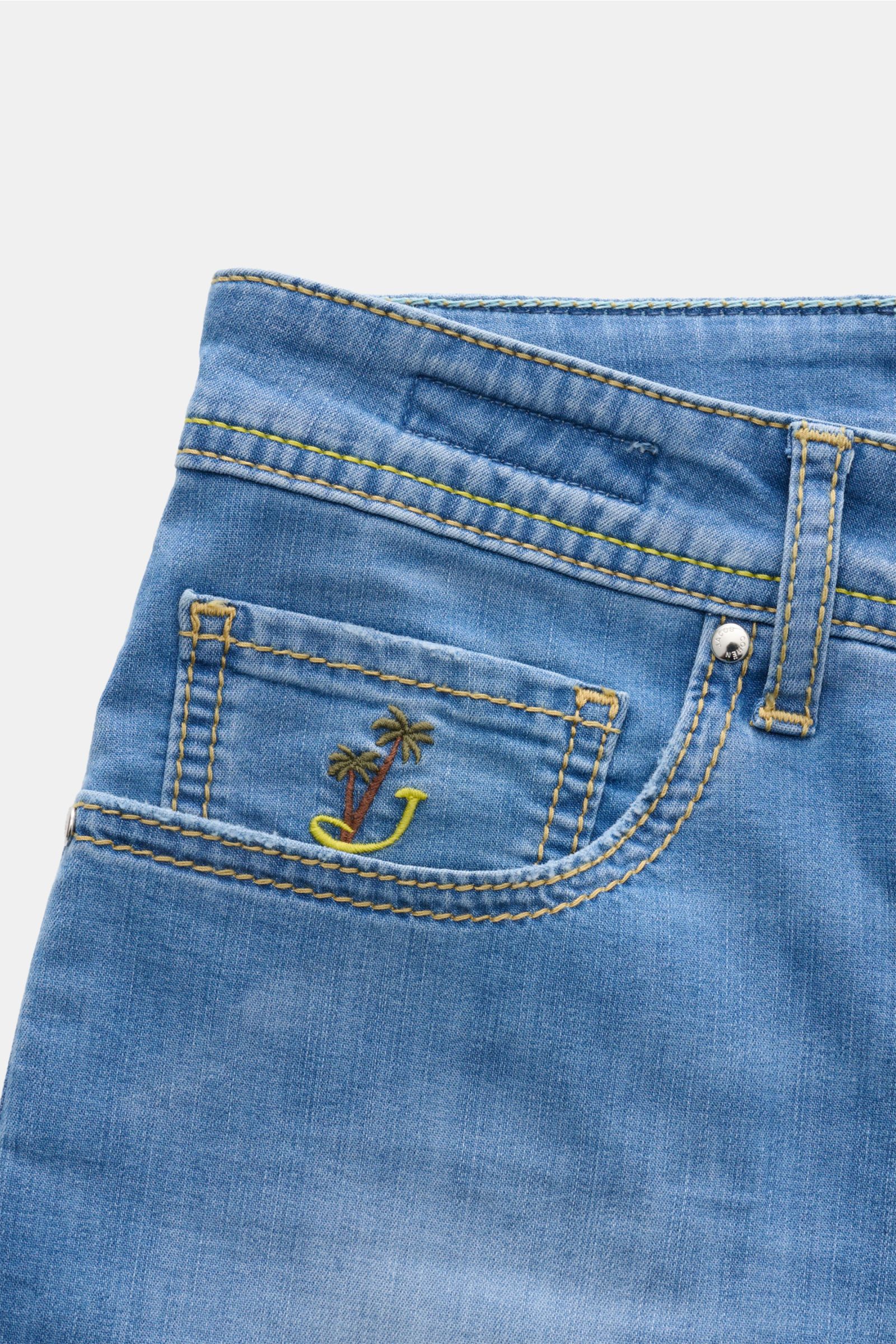Close-up front-side view of Jacob Cohen Jeans 'Bard' blau, lightweight cotton-viscose denim with elastic, soft feel, authentic used wash, slim fit, button fly, five-pocket style, palm tree embroidered coin pocket, and distinctive leather patch.