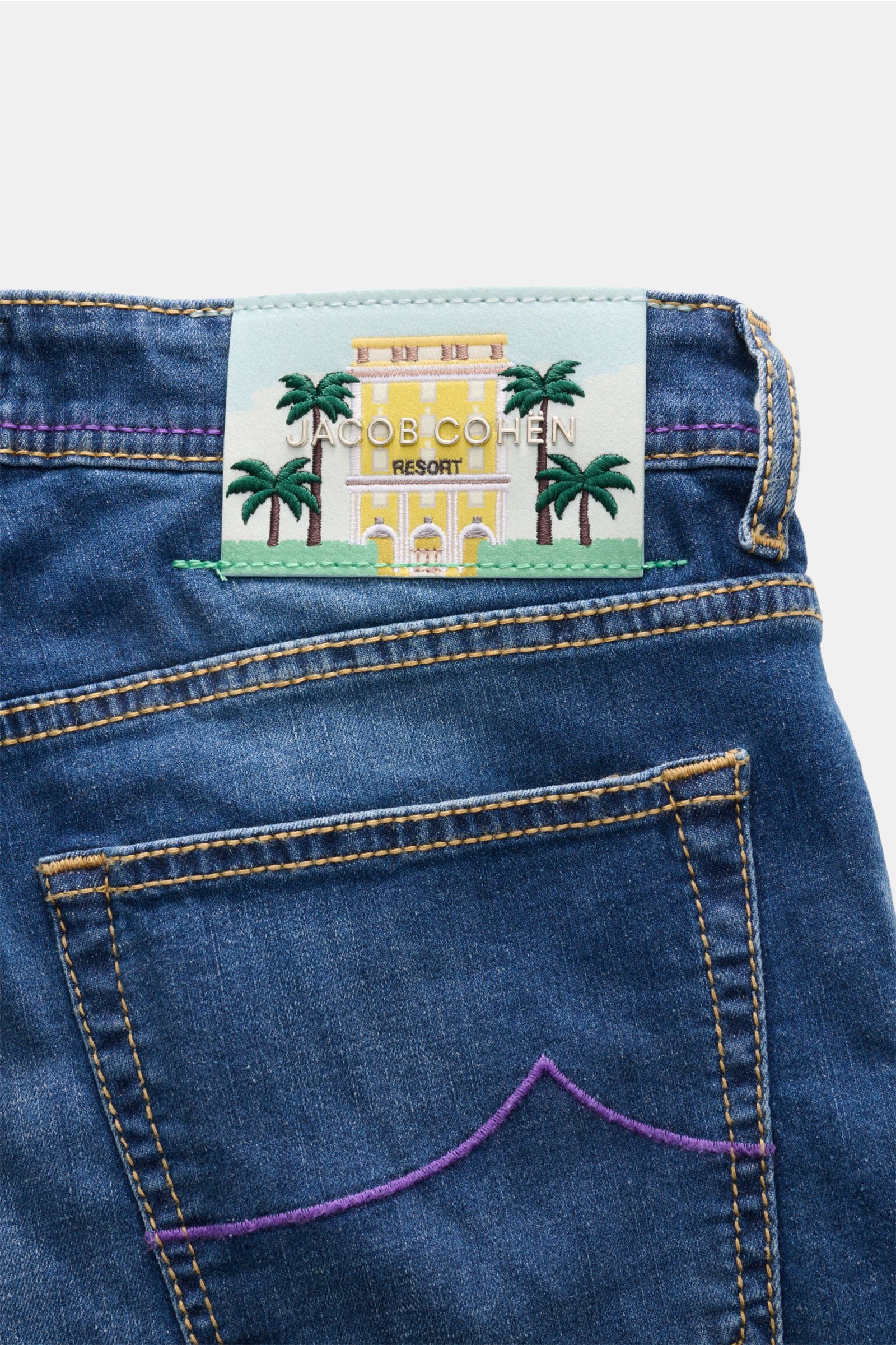 Jacob Cohen Jeans 'Bard Resort' dunkelblau, Detailaufnahme von Gesäßtasche mit lila Palmen-Stitching und Lederpatch mit Resort-Motiv.