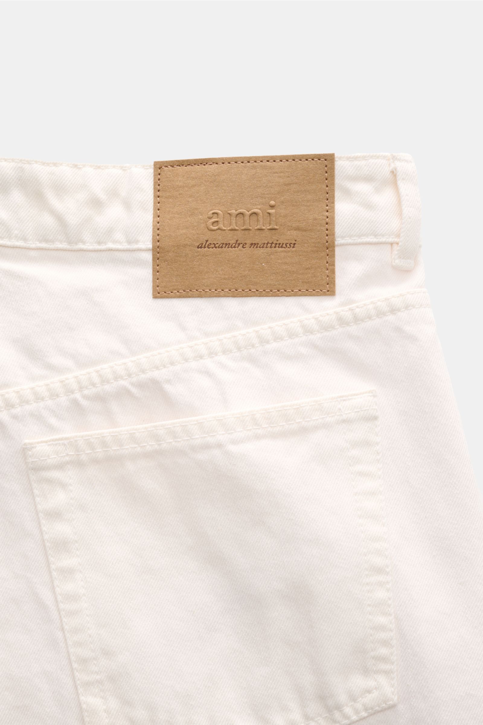 A close-up rear view of Ami Paris Jeans 'Large Fit' offwhite showing the offwhite pure cotton denim, authentic used wash, five-pocket style, button fly, loose fit, straight cut, grippy texture, and a brown logo patch. Lässige Denim vom Pariser Label AM