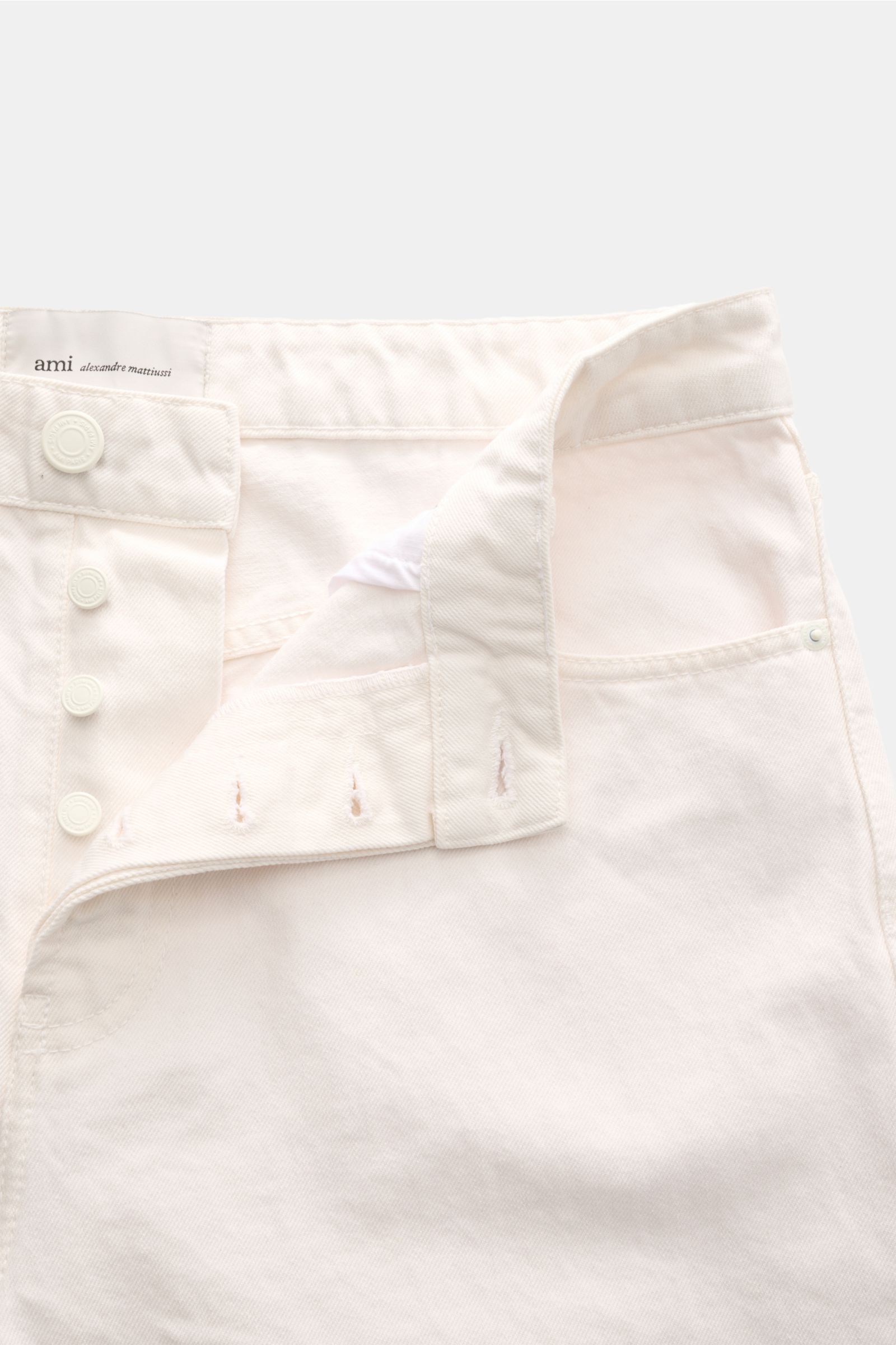 Close-up front view of Ami Paris Jeans 'Large Fit' offwhite in pure cotton denim with button fly, loose fit, and authentic used wash. 

Lässige Denim vom Pariser Label AMI PARIS: Mit dem Modell 'Large Fit' aus reinem Baumwoll-Denim sind Sie perfekt aus