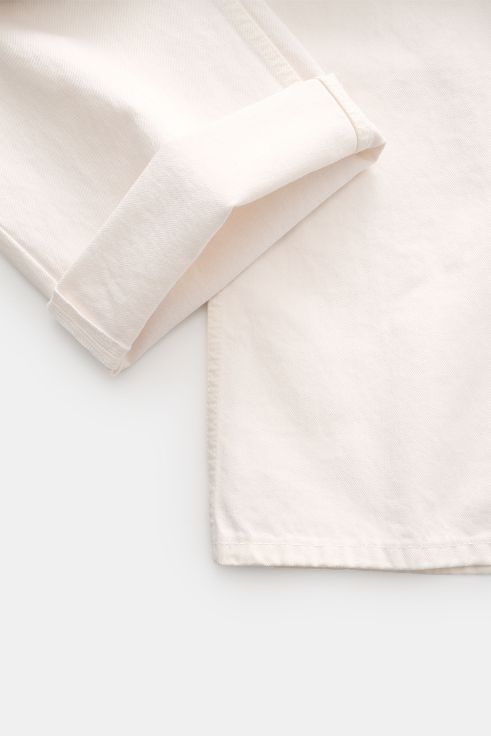 Offwhite Ami Paris Jeans 'Large Fit' shown from a close-up top-down angle focusing on the cuff and fabric texture. Lässige Denim vom Pariser Label AMI PARIS: Mit dem Modell 'Large Fit' aus reinem Baumwoll-Denim sind Sie perfekt ausgestattet, wenn es im ei