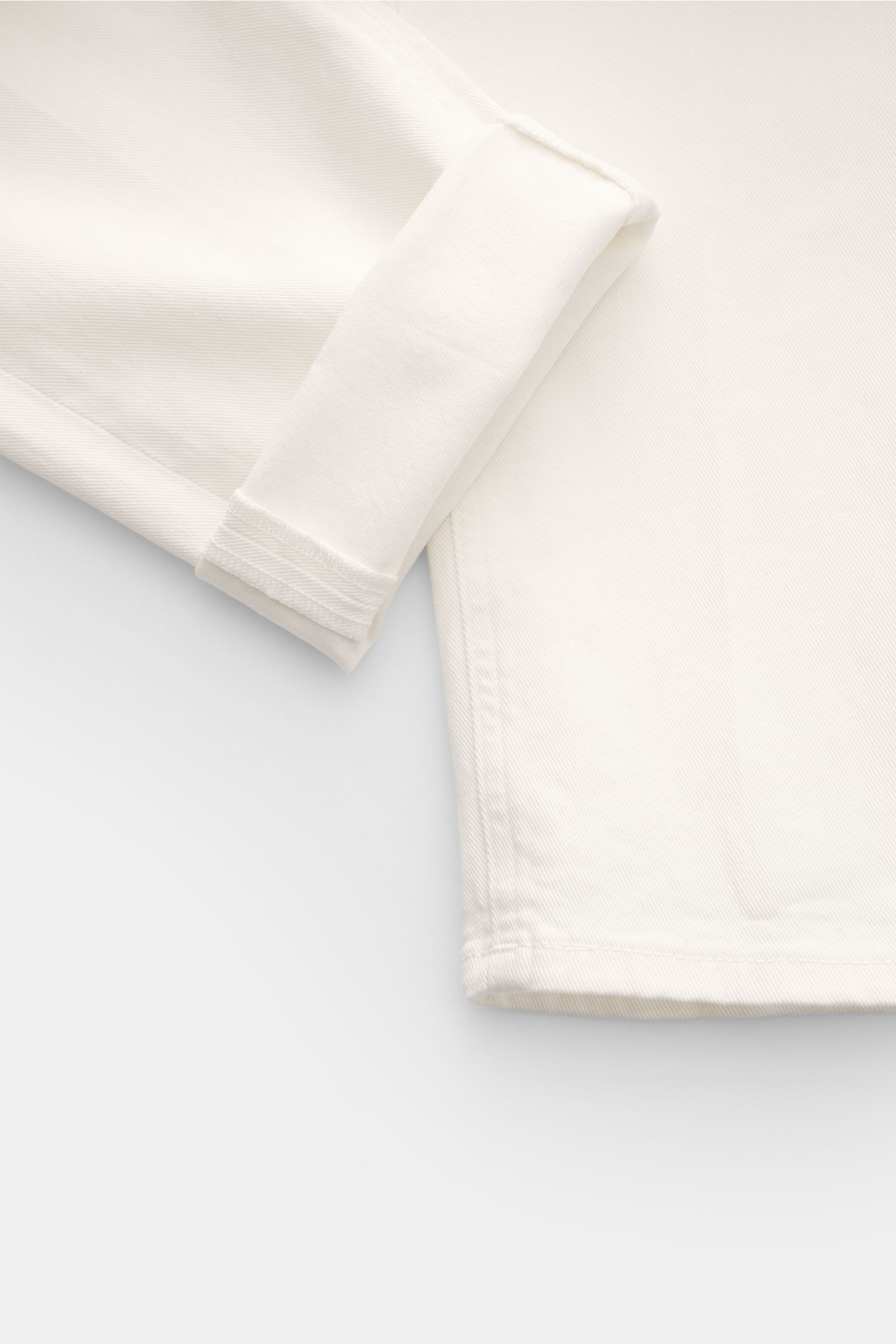 Off-white PT Torino Denim Jeans 'Reggae' cropped with slim fit, very tapered cut, short length, button fly, five-pocket style, and contrasting logo patch, shown from a close-up top-down angle focusing on the folded hem and fabric texture. 

The cropped