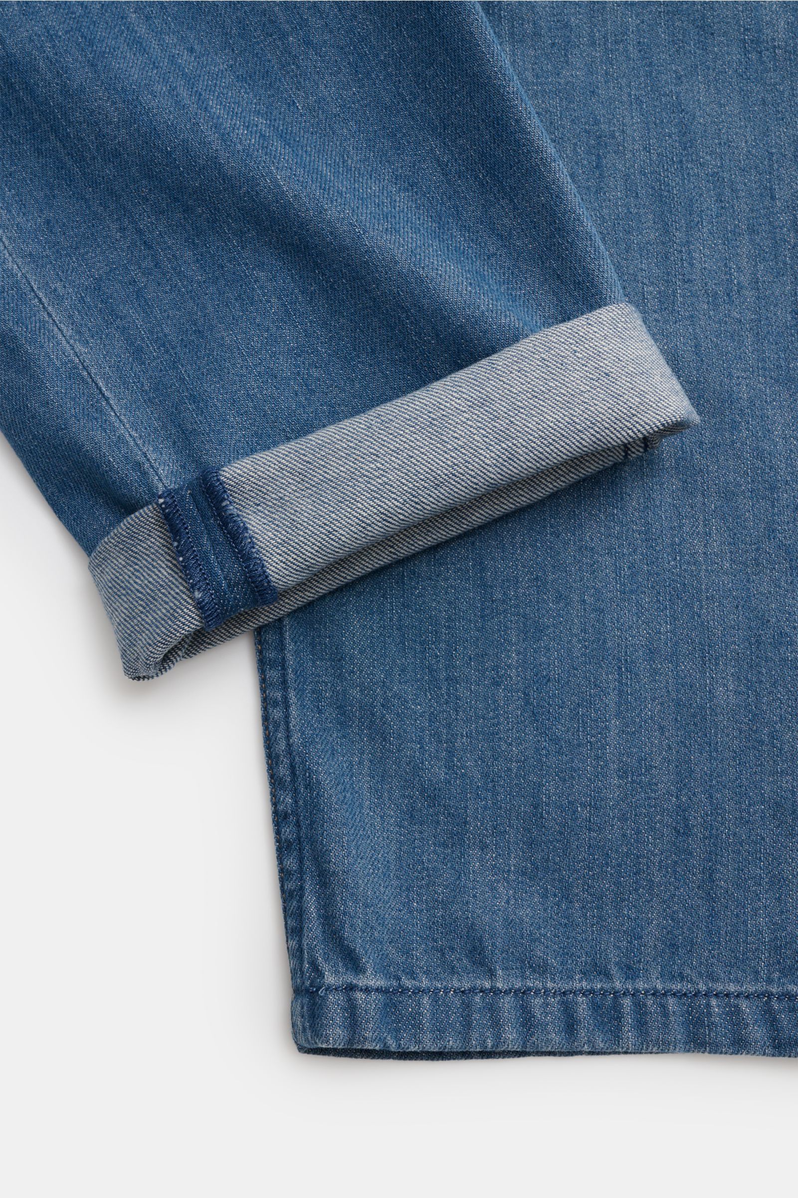 A close-up side view of the cuffed leg of A.P.C. Jeans 'Jean Martin' blau in blue denim with authentic wash, contrast stitching, and slightly textured pure cotton fabric. Mit ihrem lässigen Schnitt und der authentischen Waschung wird die 'Jean Martin' von