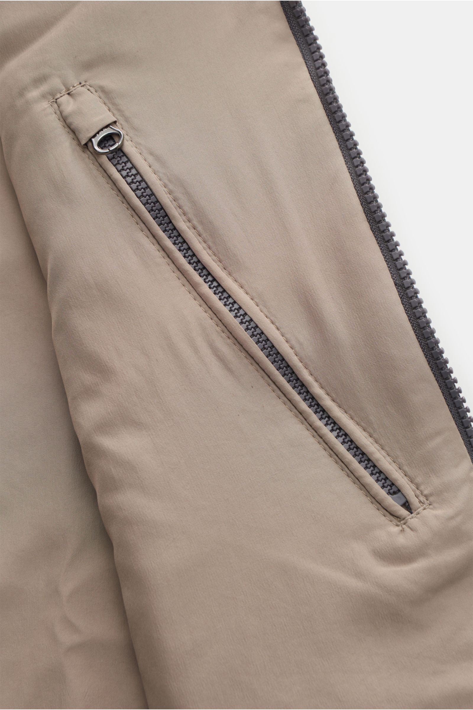 Nahaufnahme der seitlichen Leistentasche mit Reißverschluss der The Product is the Hero Daunenweste 'A Special Vest' grau meliert aus mulesingfreier Schurwolle.