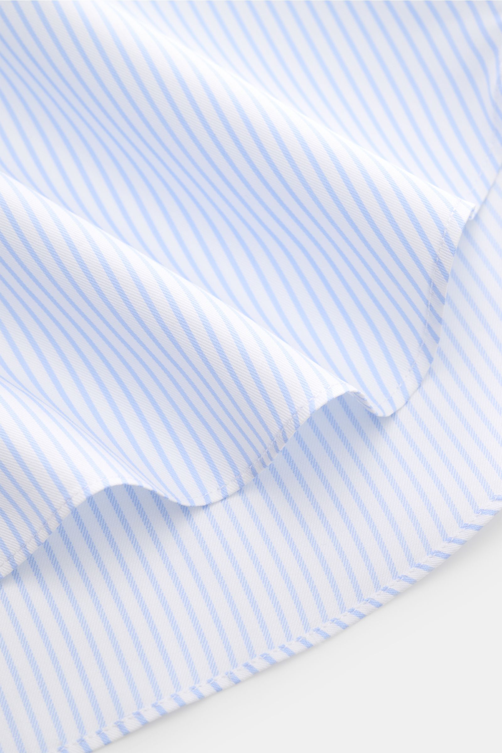 Finamore Business shirt 'Rodi Napoli' Kent collar light blue/white striped shown in close-up from an angled top view, fine cotton gabardine, smooth feel, slim fit, extra-long sleeves, Kent collar, French button placket, classic barrel cuffs, rounded hem.