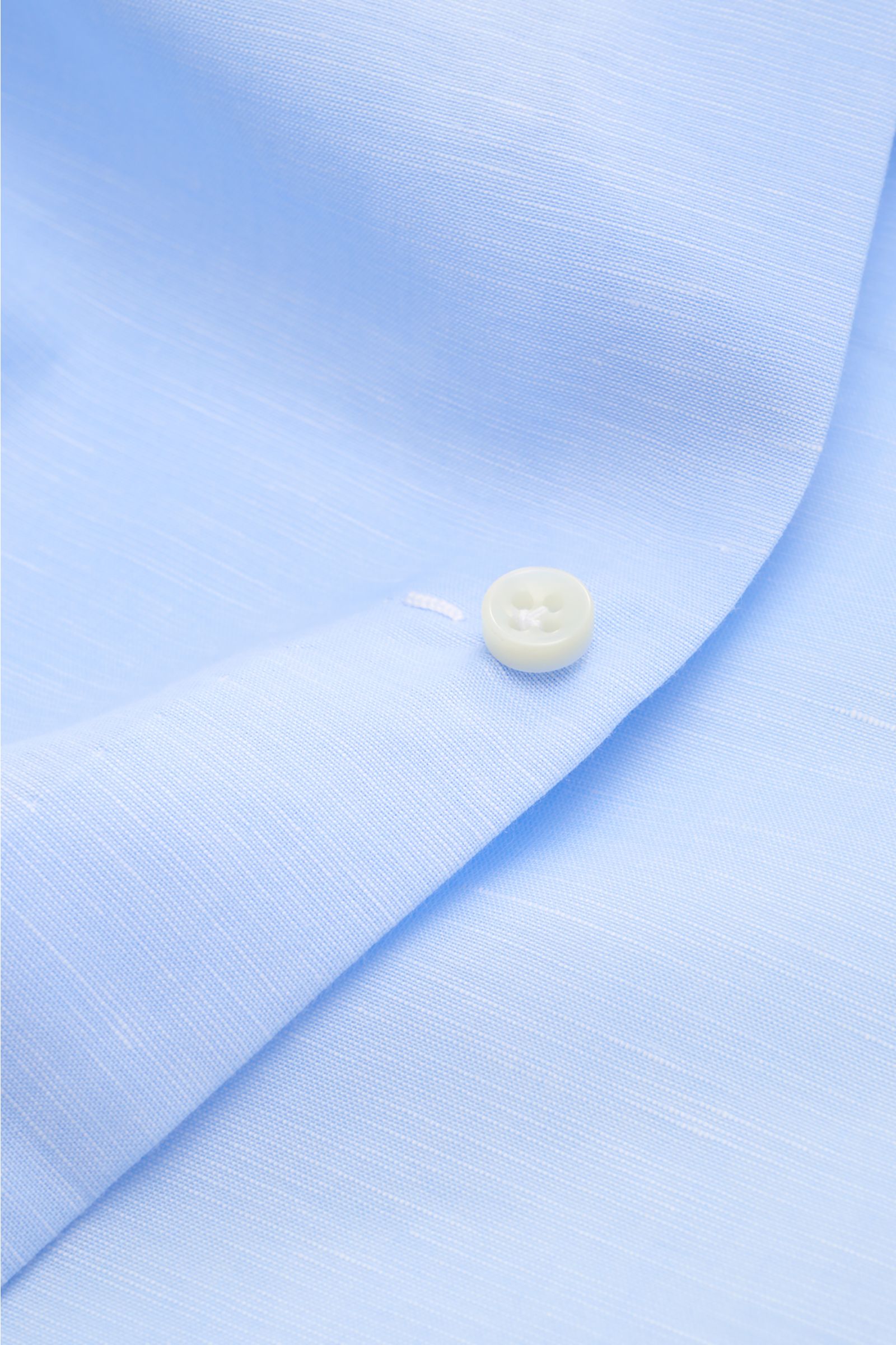 Nahaufnahme des Borrelli Business Hemd 'Luciano' Kent-Kragen hellblau aus Leinen-Baumwoll-Mix mit Perlmuttknopf, glattem Griff und Slim Fit, fotografiert aus schräger Perspektive.