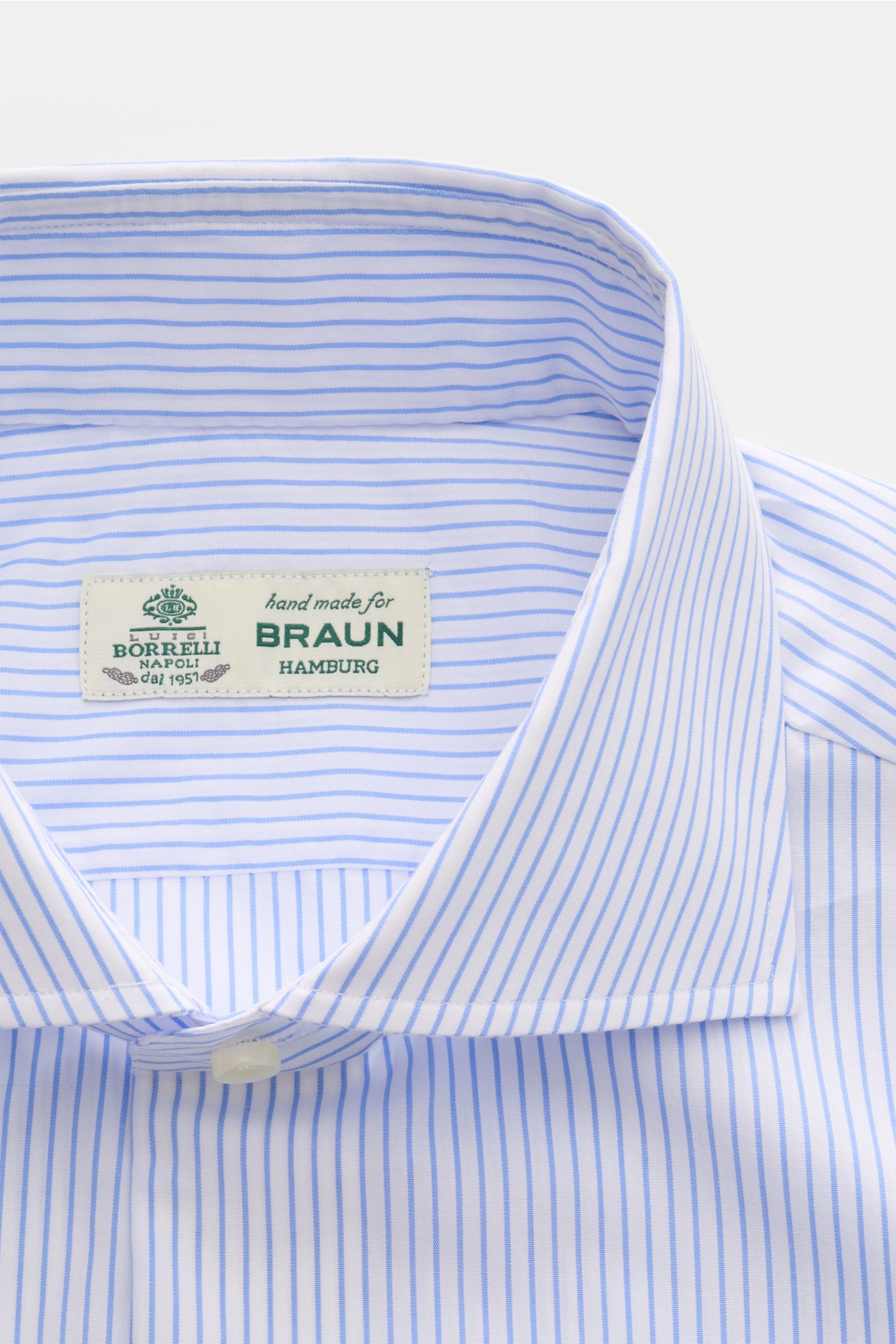 Nahaufnahme des Borrelli Business Hemd 'Nando' Haifisch-Kragen blau/weiß gestreift, Slim Fit, reine Baumwolle, weiche Qualität, französische Knopfleiste mit Perlmuttknöpfen, klassische Sportmanschette, gerundeter Saum, fotografiert von oben.