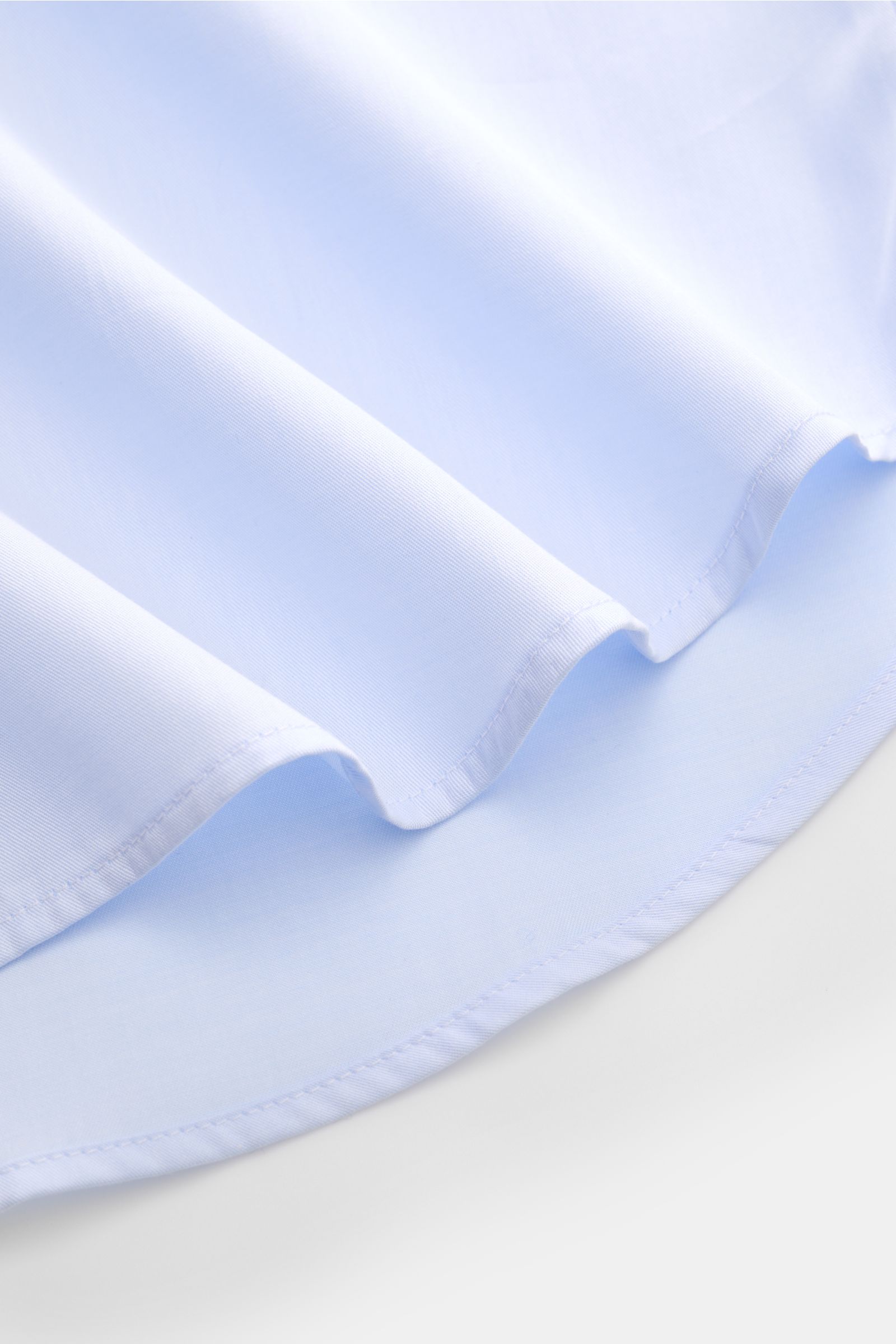 Nahaufnahme des gerundeten Saumverlaufs vom BRAUN Hamburg Business Hemd Haifisch-Kragen hellblau aus feiner Baumwoll-Gabardine mit glattem Griff.