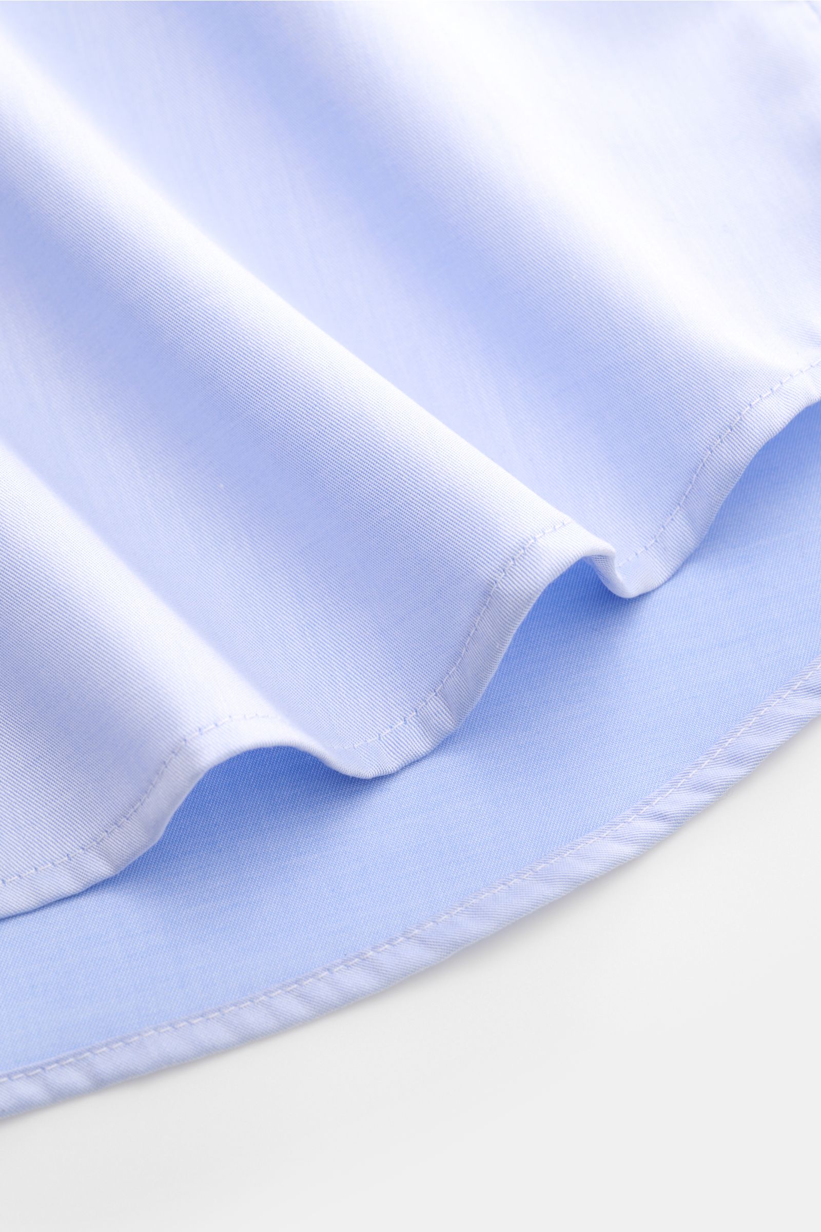 Nahaufnahme des gerundeten Saumverlaufs vom BRAUN Hamburg Business Hemd Haifisch-Kragen hellblau aus feiner Baumwoll-Gabardine, weicher Griff, Extra Slim Fit, französische Knopfleiste, klassische Sportmanschette, rückwärtige Taillenabnäher.