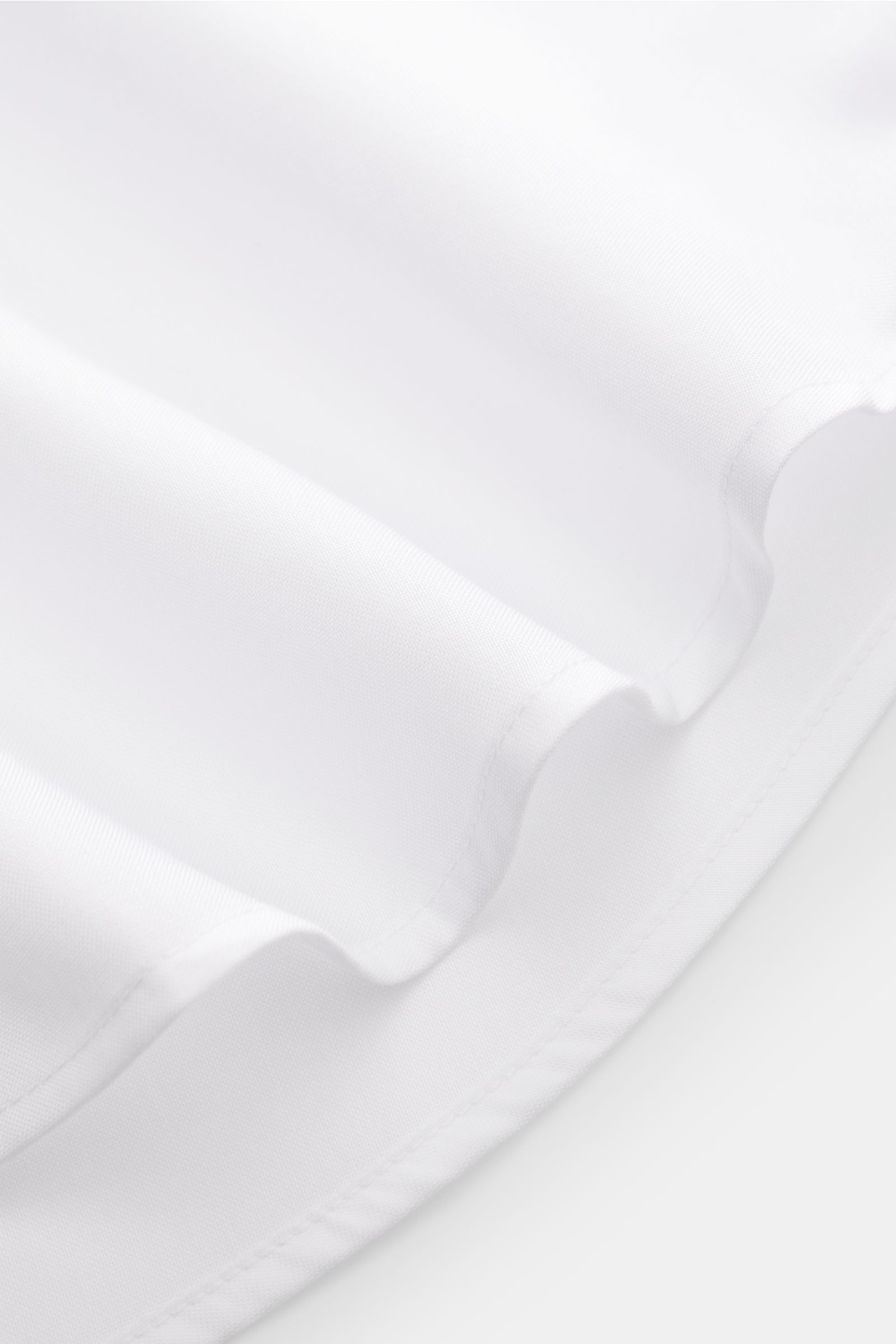 Nahaufnahme des gerundeten Saumverlaufs vom BRAUN Hamburg Business Hemd Haifisch-Kragen weiß, feiner Baumwoll-Pinpoint, glatter Griff, Extra Slim Fit, französische Knopfleiste, klassische Sportmanschette.