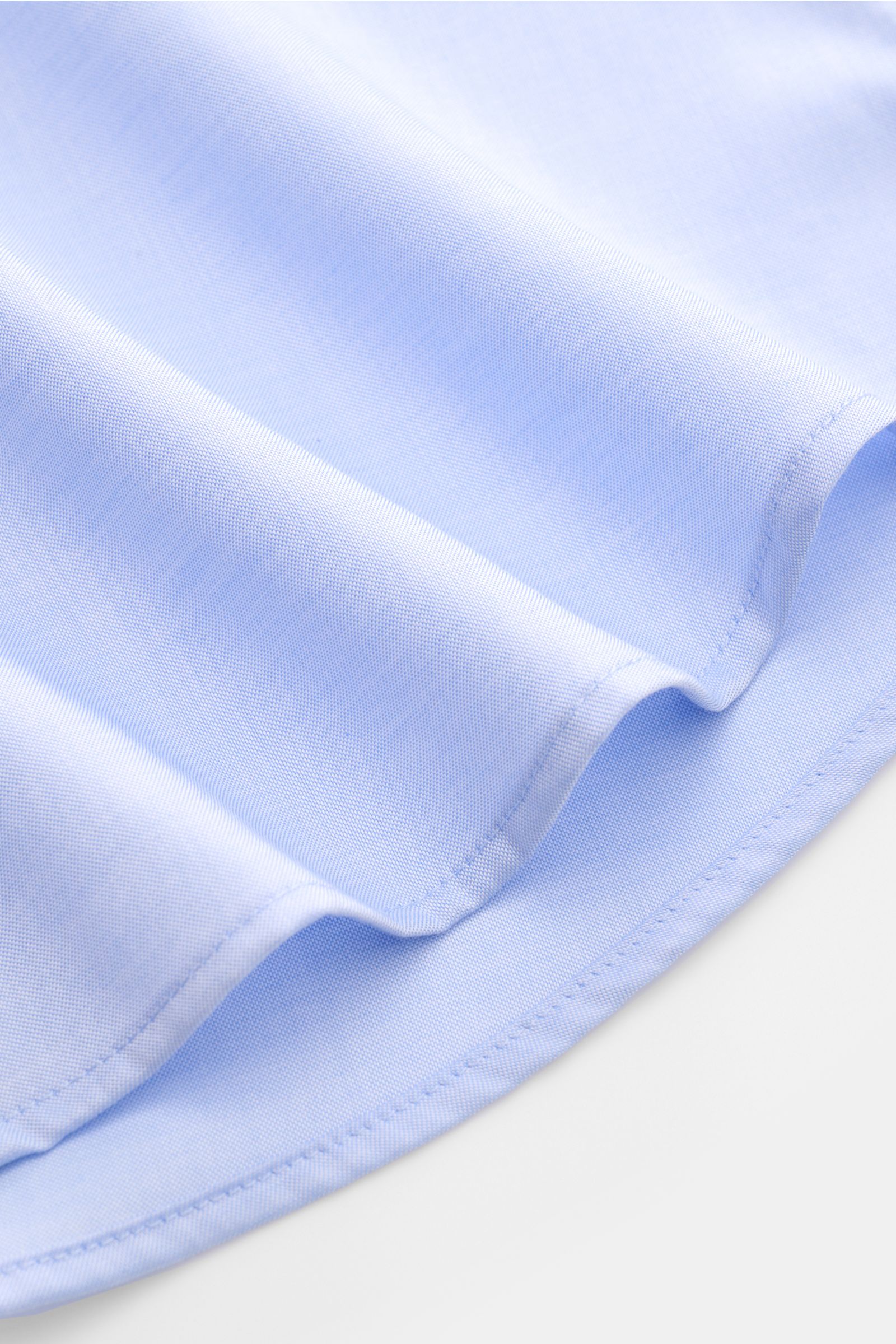 Nahaufnahme des gerundeten Saumverlaufs vom BRAUN Hamburg Business Hemd Haifisch-Kragen hellblau, feiner Gabardine aus Baumwolle, weicher Griff, Extra Slim Fit, französische Knopfleiste, klassische Sportmanschette und rückwärtige Taillenabnäher sichtbar.
