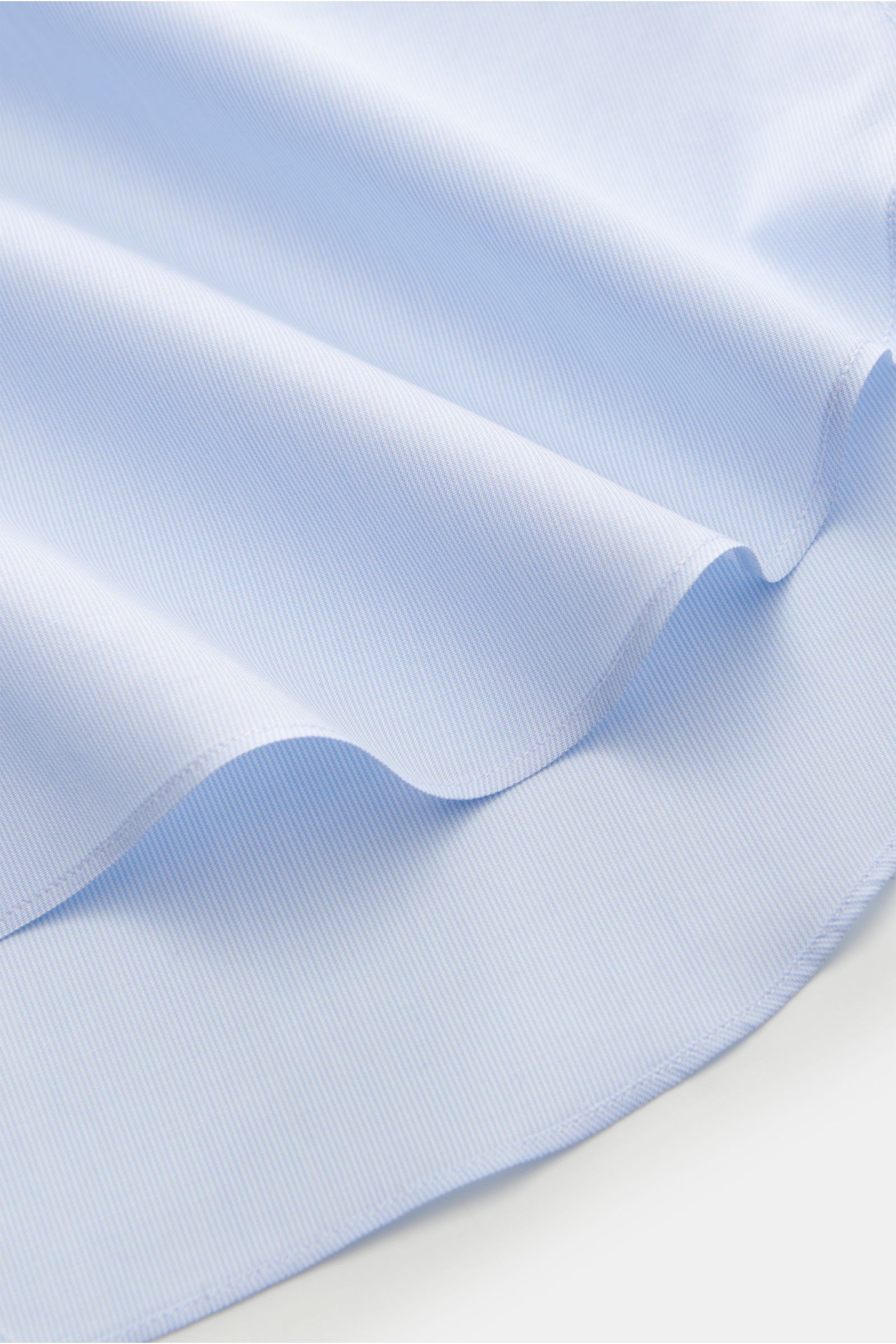 Close-up front-angle view of the Finamore Business Hemd 'Sergio Napoli' Haifisch-Kragen hellblau/weiß gestreift, showcasing fine light blue and white stripes in a smooth poplin cotton fabric with a rounded hem.

Zeitloser Klassiker aus feiner Baumwolle