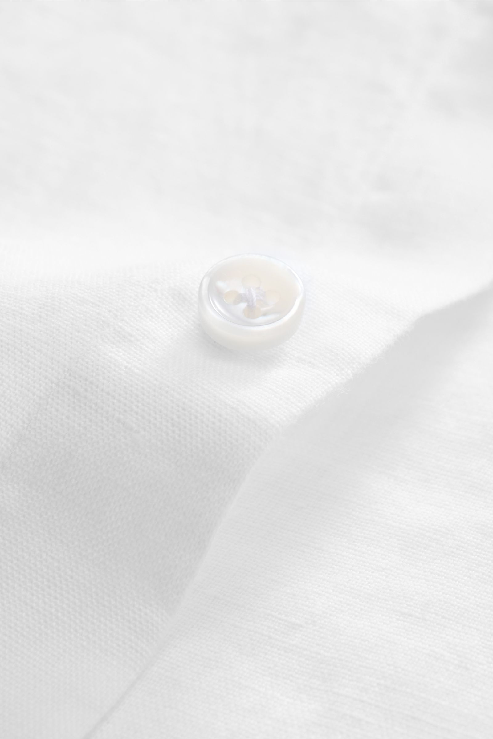 Nahaufnahme eines weißen Knopfes auf dem von Braun Leinenhemd Haifisch-Kragen weiß, zeigt die feine Leinenstruktur, reine Qualität, weicher Griff, luftige Slim-Fit-Perspektive.