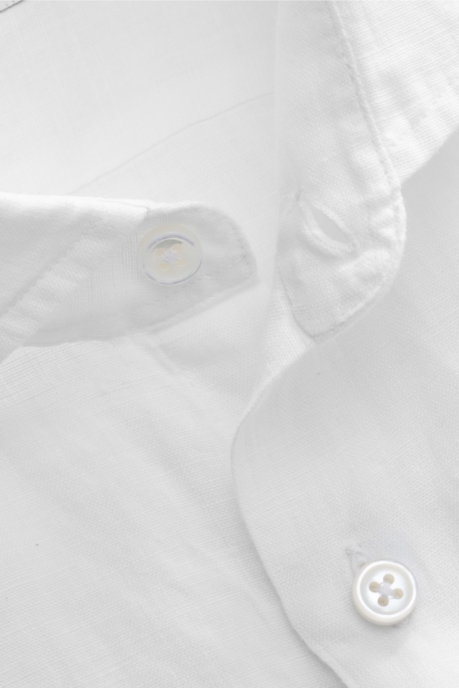 Nahaufnahme aus schräger Perspektive eines weißen von Braun Leinenhemds Haifisch-Kragen mit Knopf, reines Leinen, Slim Fit, luftige Qualität.