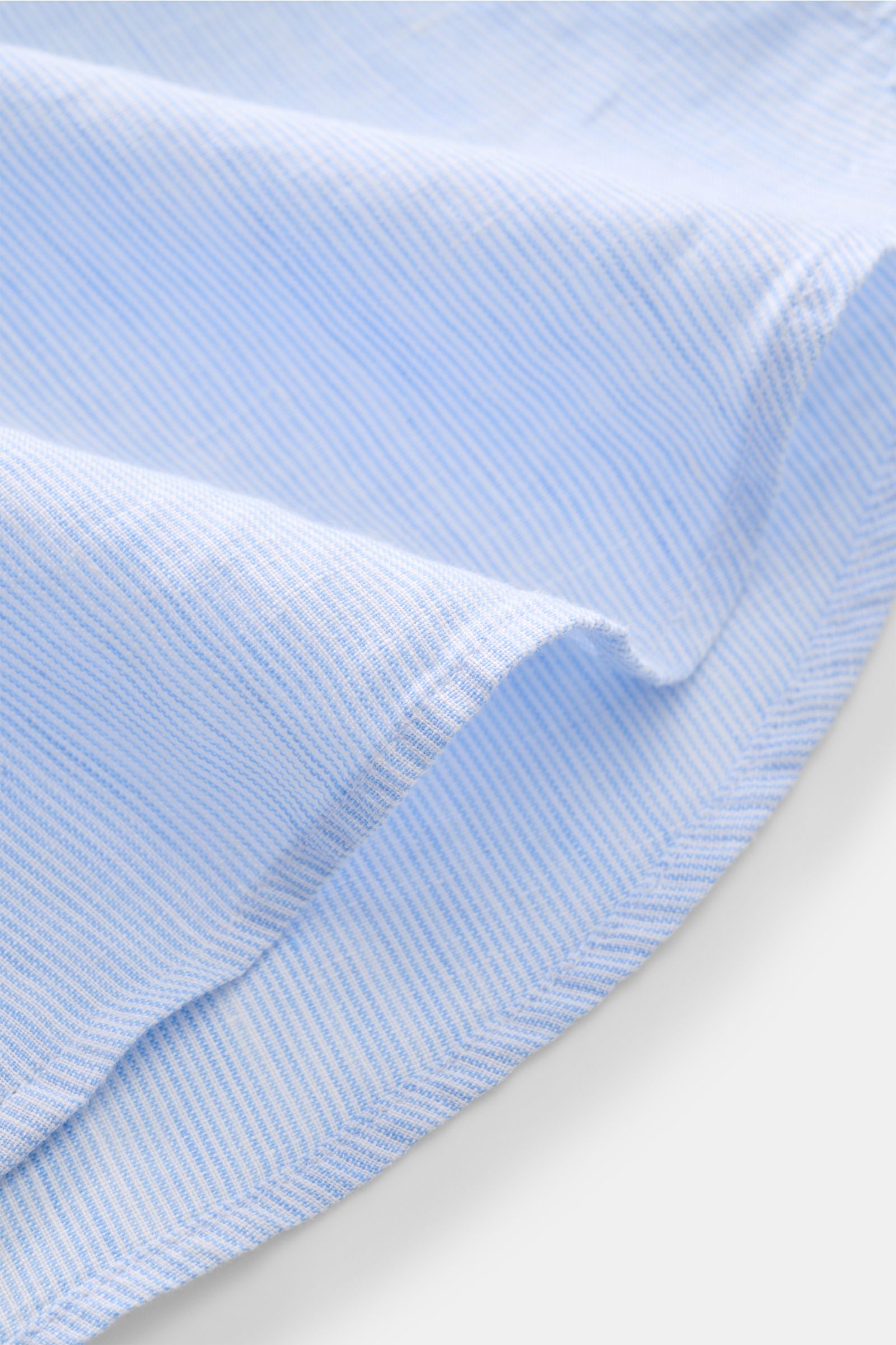 Close-up, angled view of light blue and white striped fabric showing the fine texture of the von Braun Leinenhemd Haifisch-Kragen hellblau/weiß gestreift, made from pure linen. Mühelose Leichtigkeit: Dieses VON BRAUN Hemd aus reinem Leinen überzeugt mit l