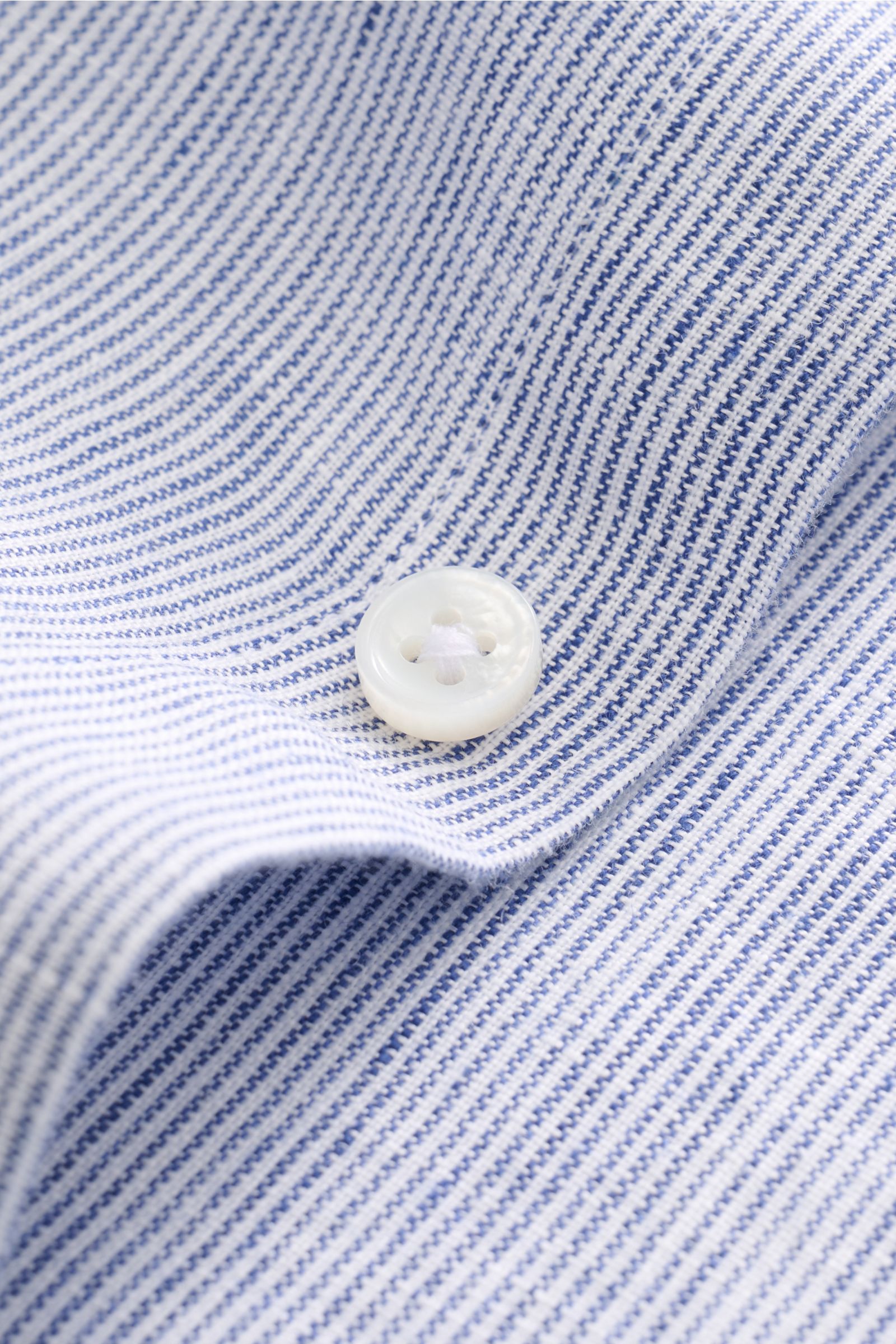 Close-up, top-down view of von Braun Leinenhemd Haifisch-Kragen navy/weiß gestreift showing white button on pure linen fabric with fine navy and white stripes, airy texture, and soft grip, highlighting its slim fit, shark collar, and classic sport cuff fo