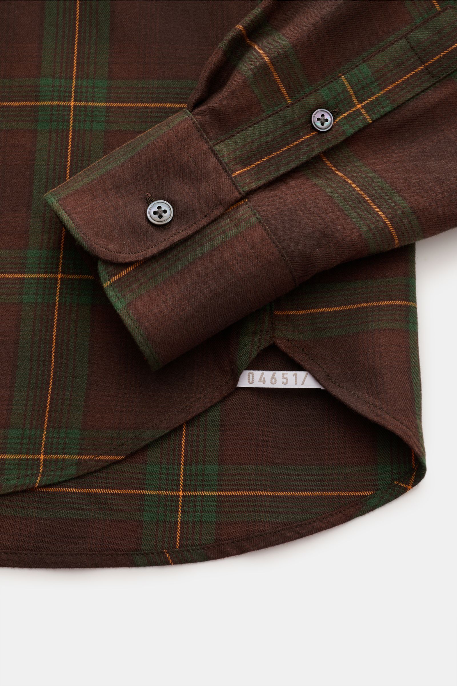 Close-up image from above showing the cuff and hem of the 04651/ A trip in a bag Flanellhemd Kent-Kragen braun/dunkelgrün/bordeaux kariert, a casually cut brown plaid flannel shirt with green and bordeaux checks. Dieses lässig geschnittene Flanellhemd 
